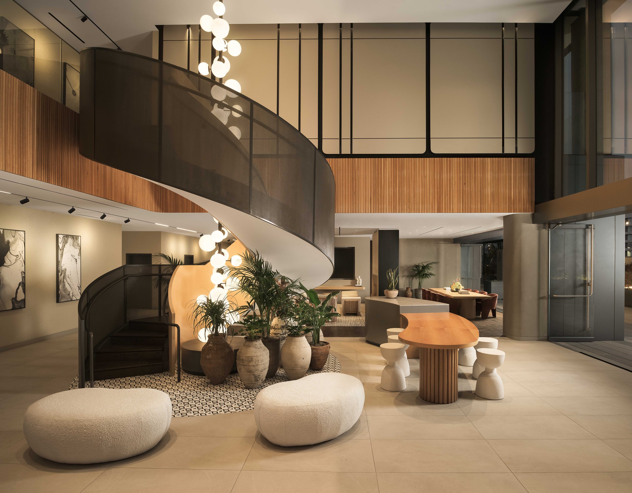 Full lobby view with curved staircase, globe pendant sculpture, and abundant tropical greenery — contemporary architecture photography, Los Angeles CA