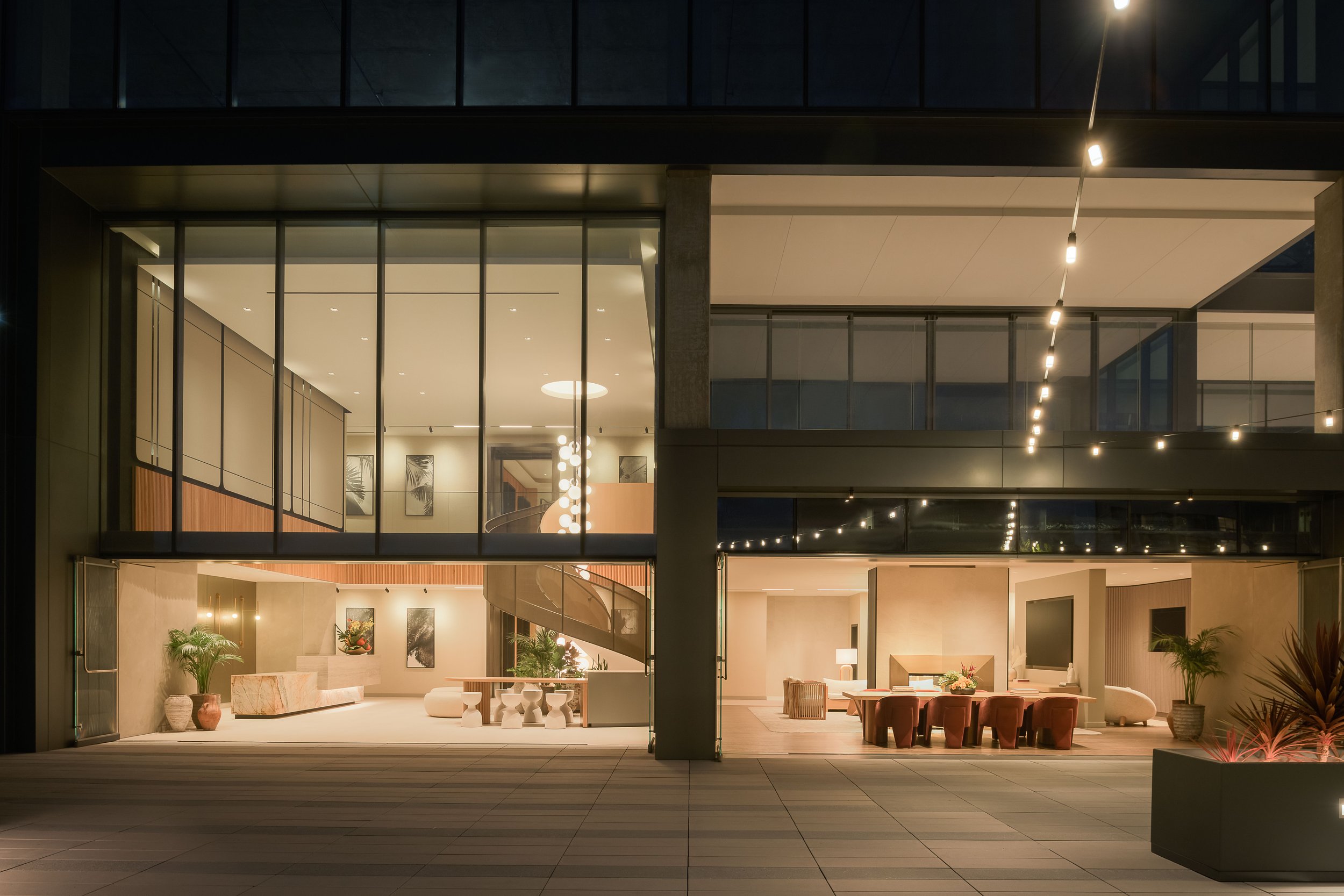 Building exterior at night viewed through glass, warm lobby glow and street-level retail — commercial architecture photography, Entrada Los Angeles CA