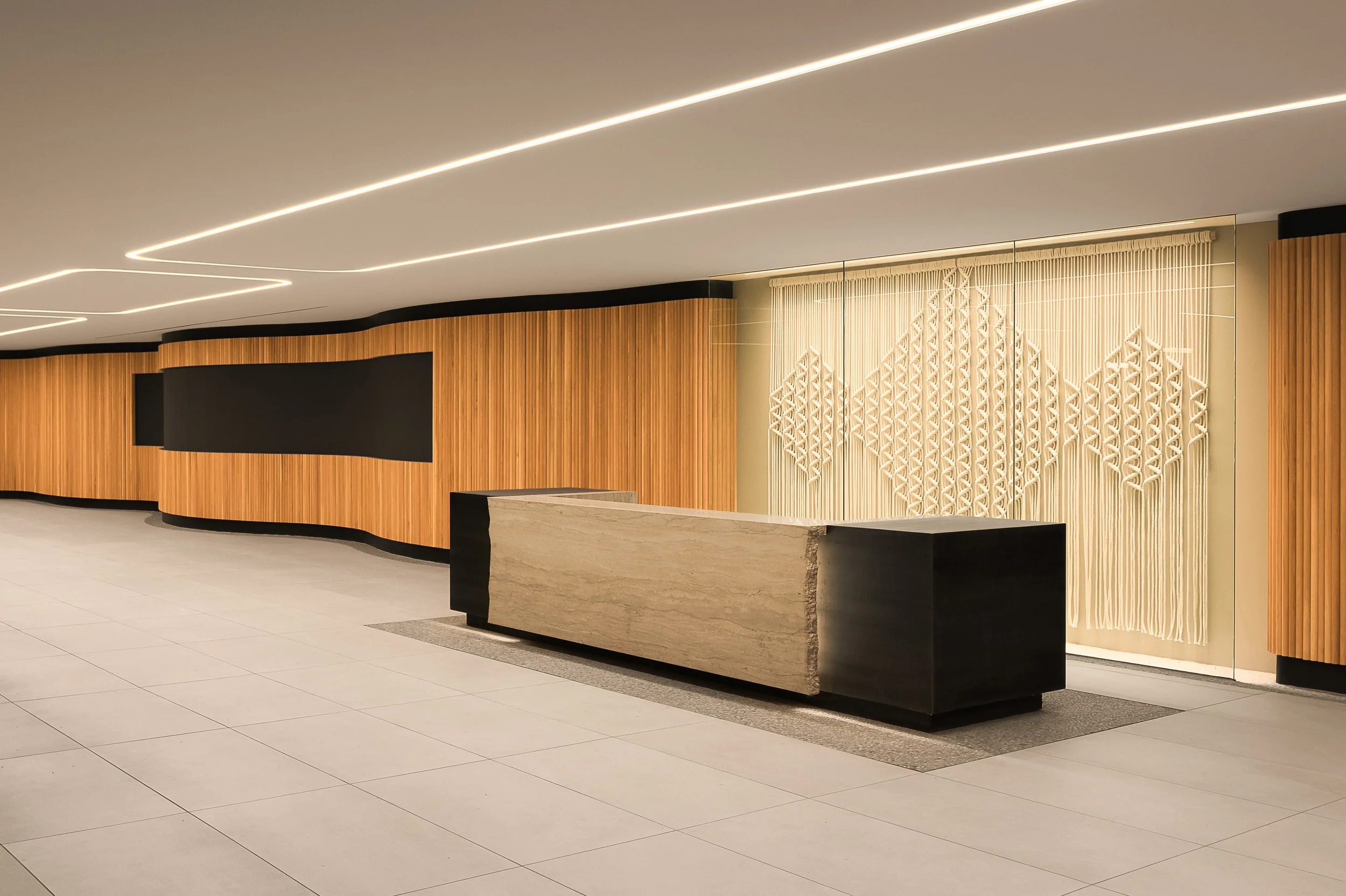 Main building reception with stone desk, curved wood slat wall, and macrame textile art — commercial interior design photography, Entrada Los Angeles CA