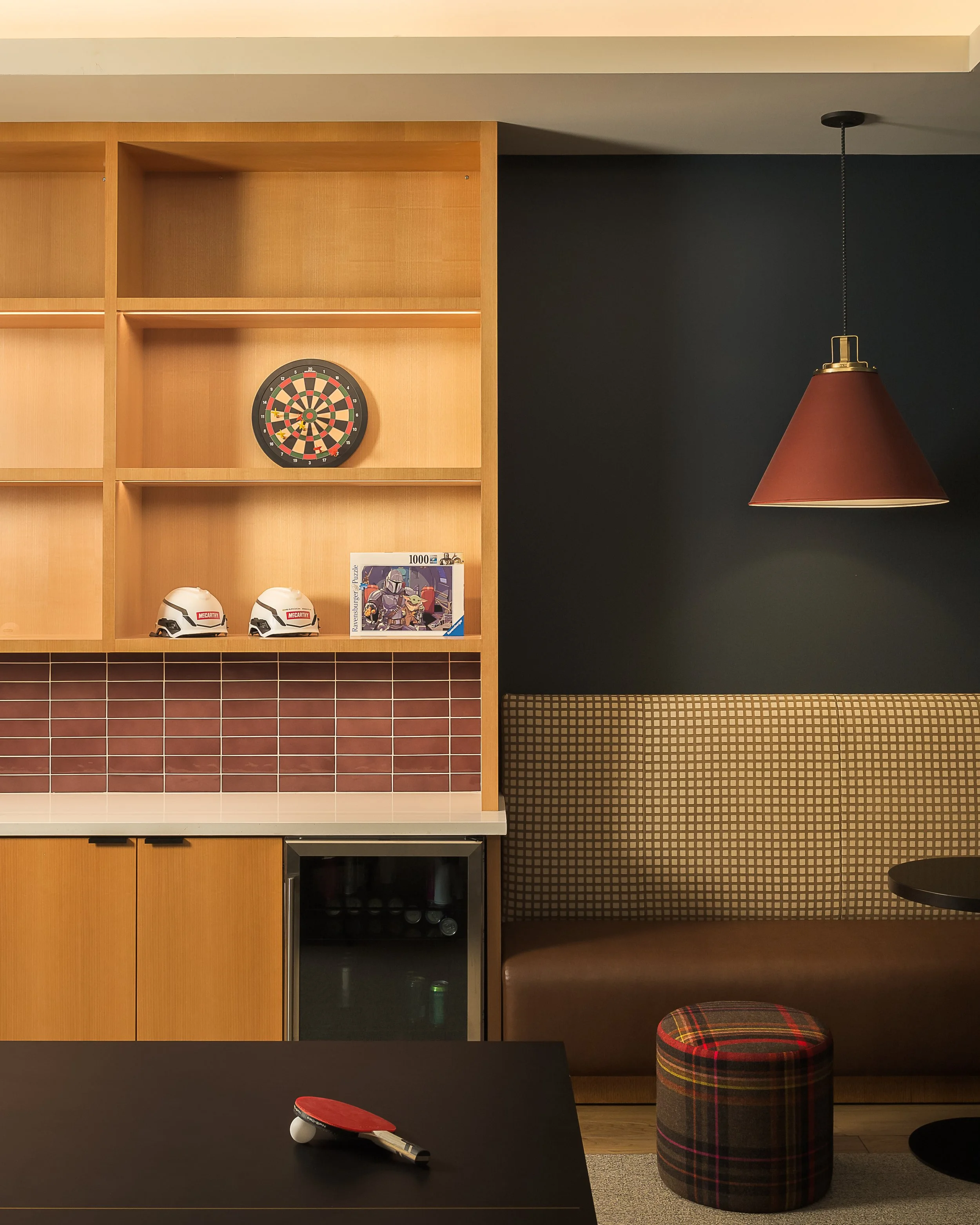 Employee fun room with dartboard, built-in wood shelving, and warm copper pendant lighting — corporate amenity interior photography, Richardson TX