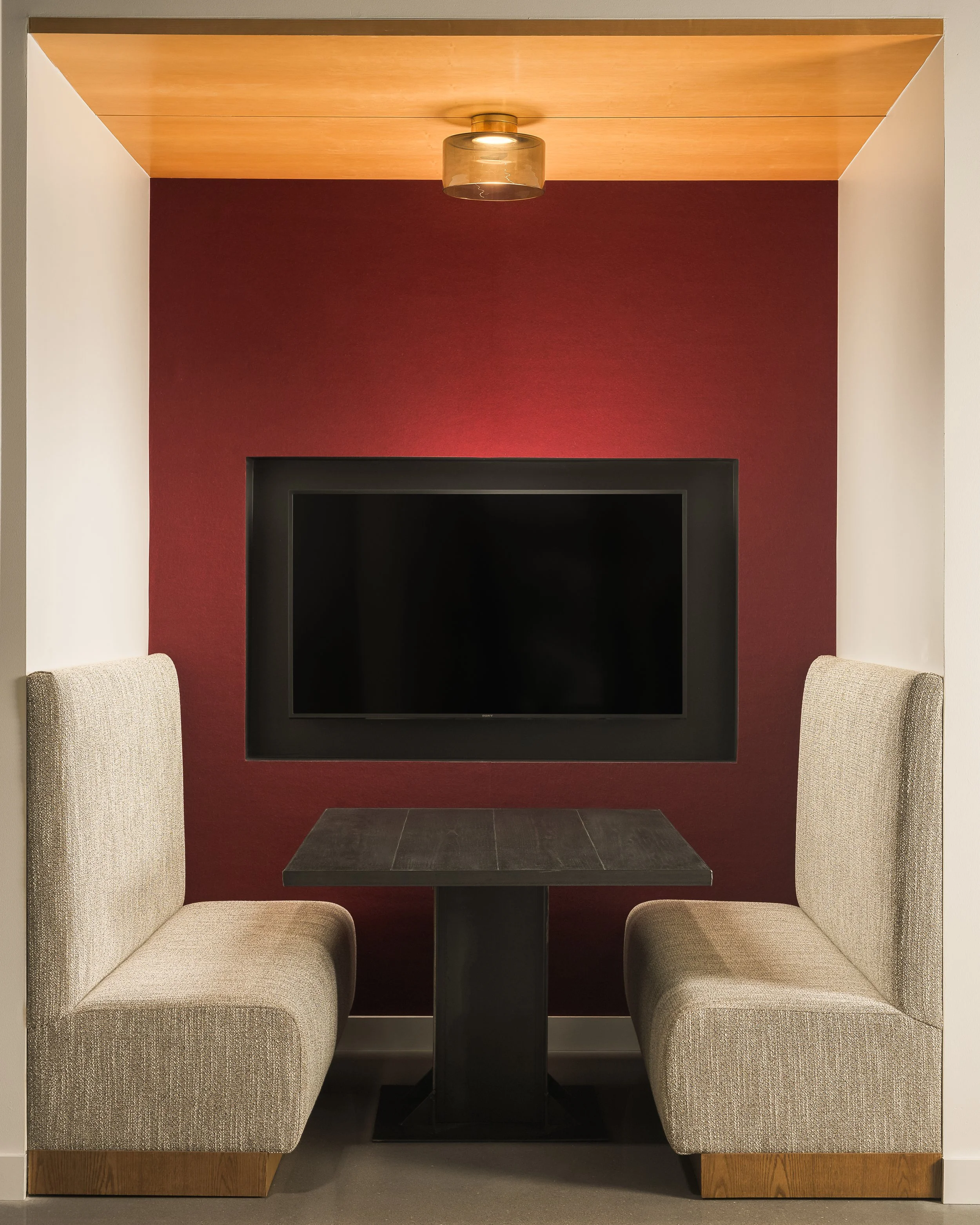 Corporate media lounge with dark red accent wall, large flat screen TV, and patterned upholstered seating — commercial interior photography, McCarthy Richardson TX