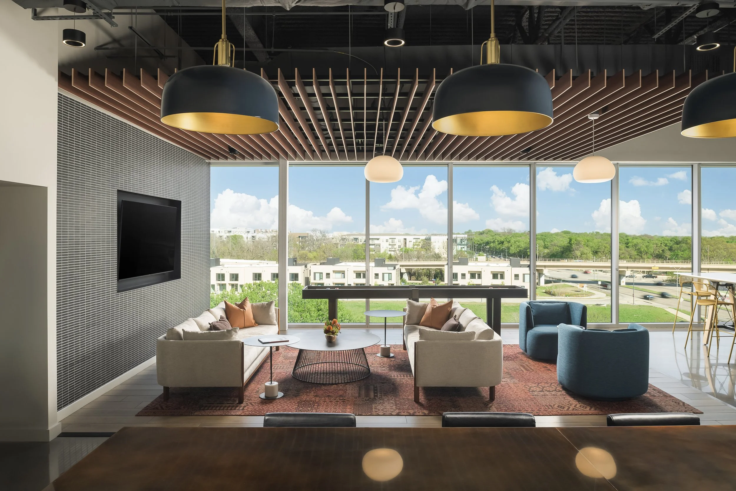 Corporate lounge area with warm pendant lighting, layered rugs, and daylit outdoor views — commercial interior design photography, McCarthy Building Companies TX