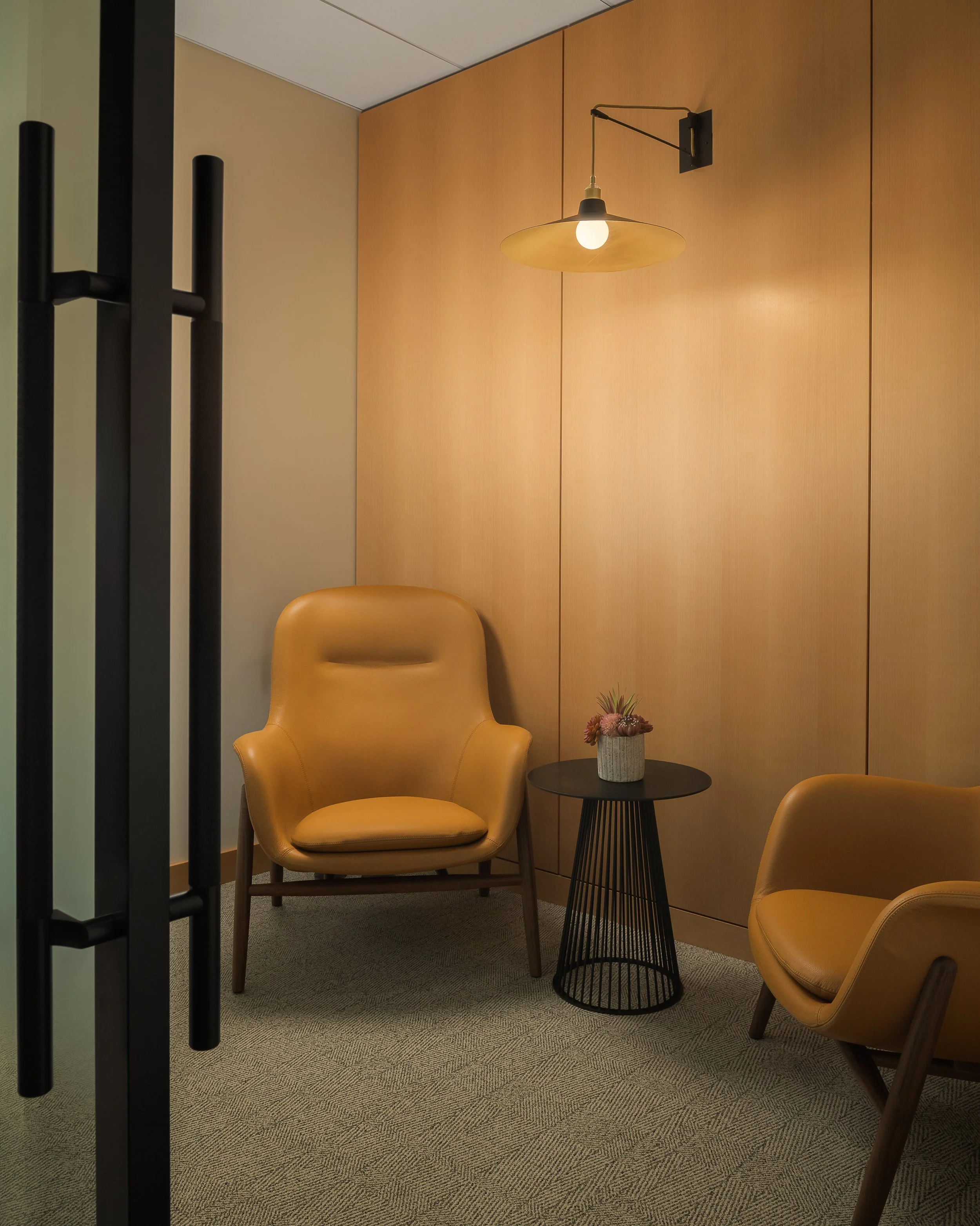 Private office nook with warm amber pendant light and caramel leather lounge chairs — corporate interior design photography, McCarthy Building Companies TX