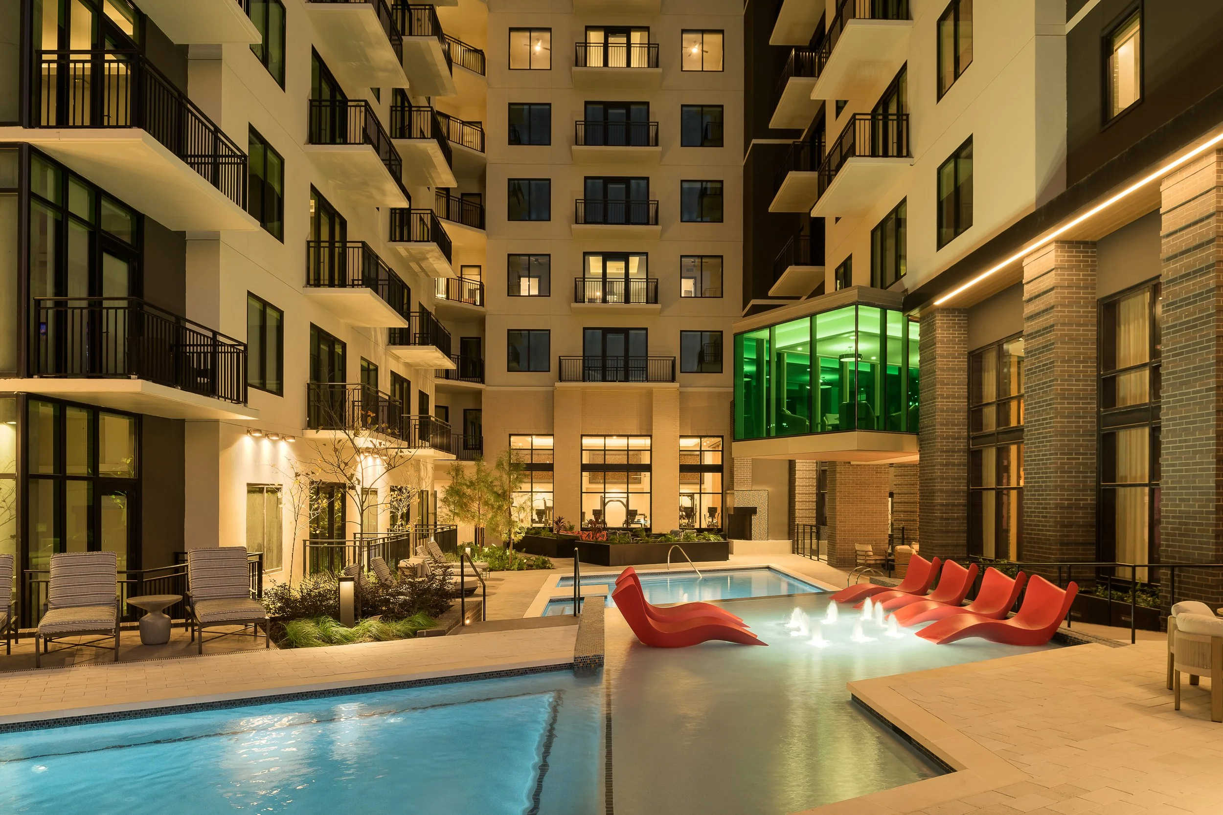 Outdoor pool courtyard with green architectural accent lighting and lounge seating — luxury apartment amenity photography, Dallas TX