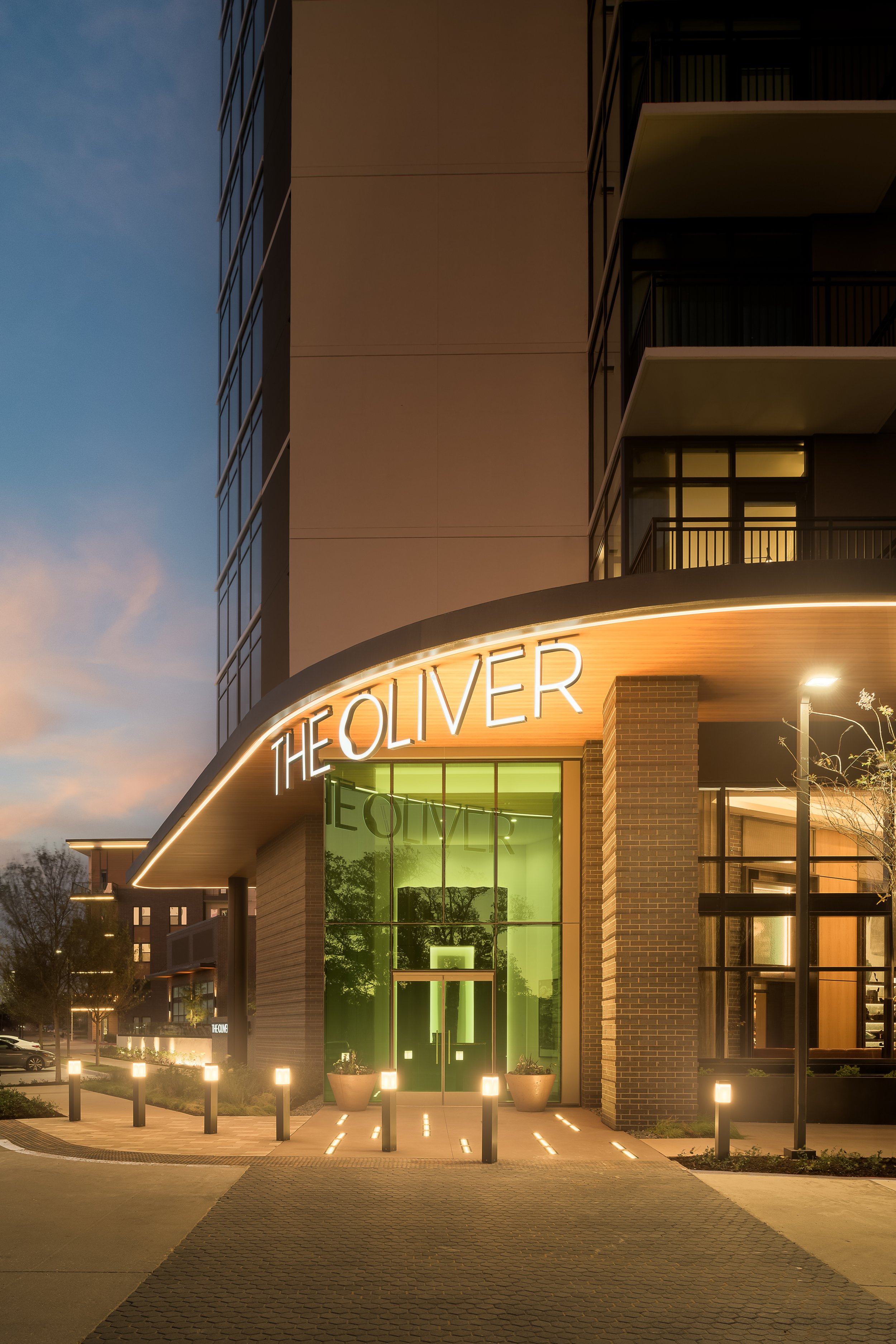 Contemporary residential building entrance at dusk with branded illuminated canopy — commercial architecture photography, The Oliver Dallas TX