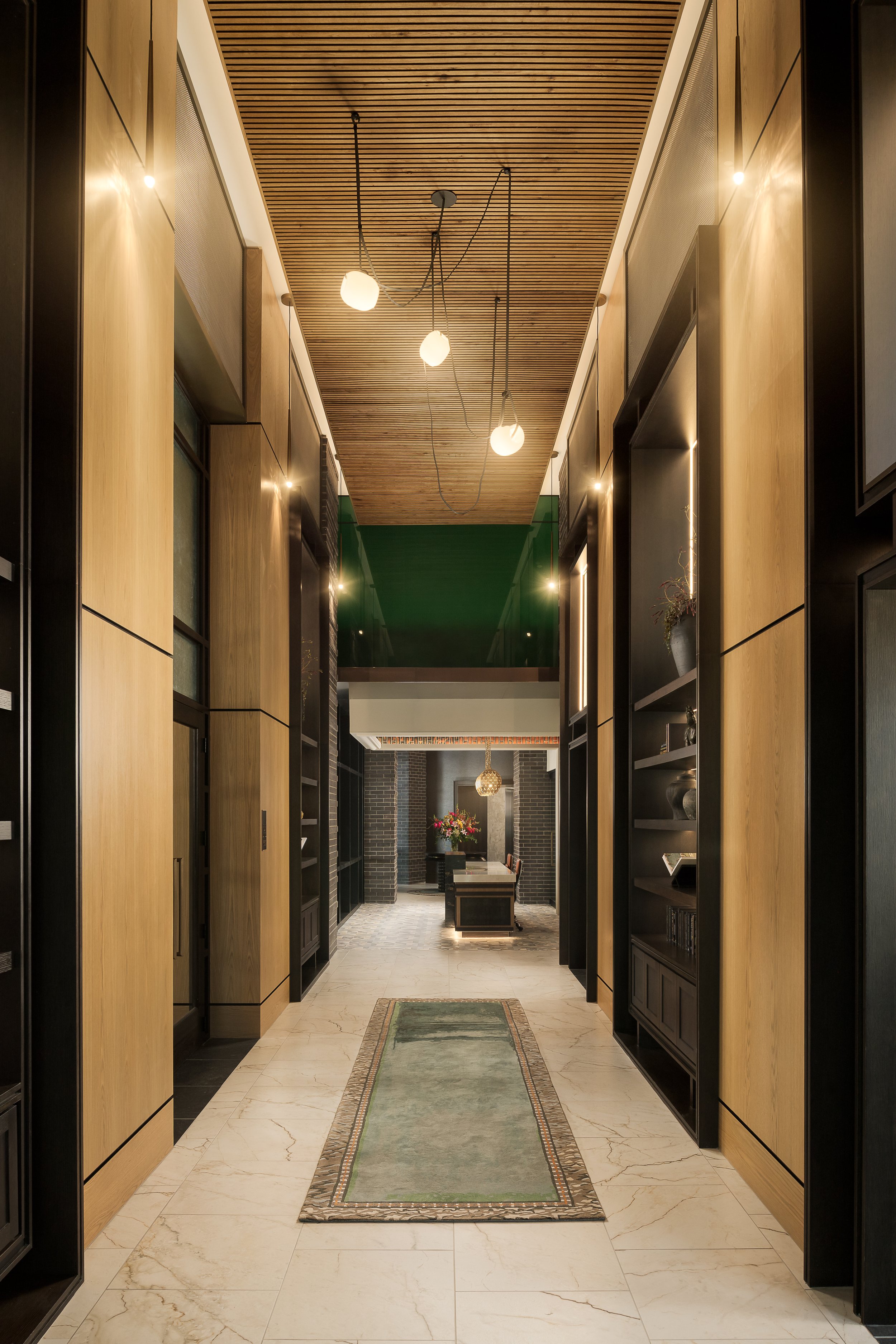 Wood-paneled amenity corridor with pendant lighting and green architectural accent — luxury apartment interior design, The Oliver Dallas TX
