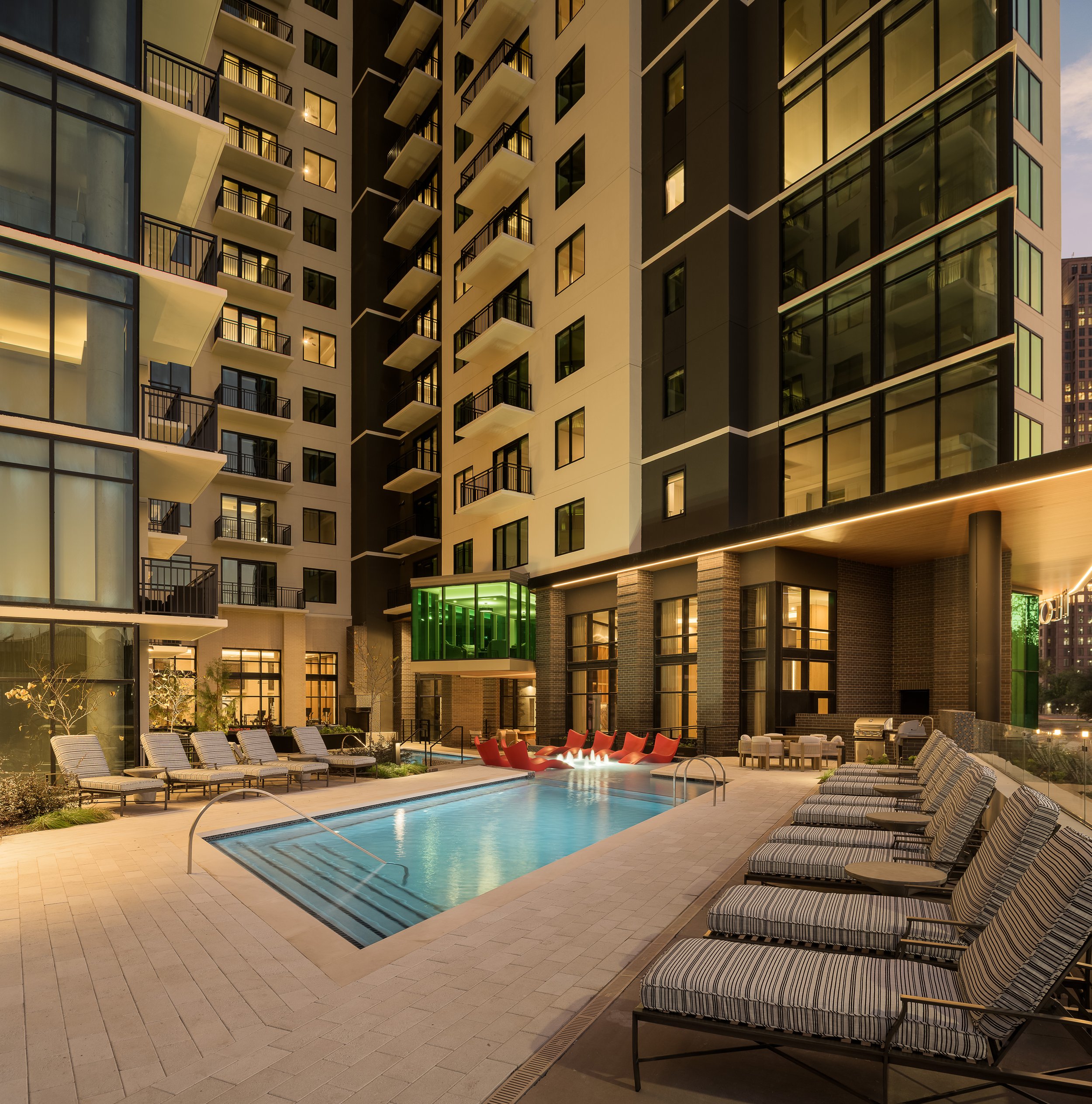 Pool deck at night with striped lounge chairs and contemporary residential building surround — luxury apartment photography, The Oliver Dallas TX