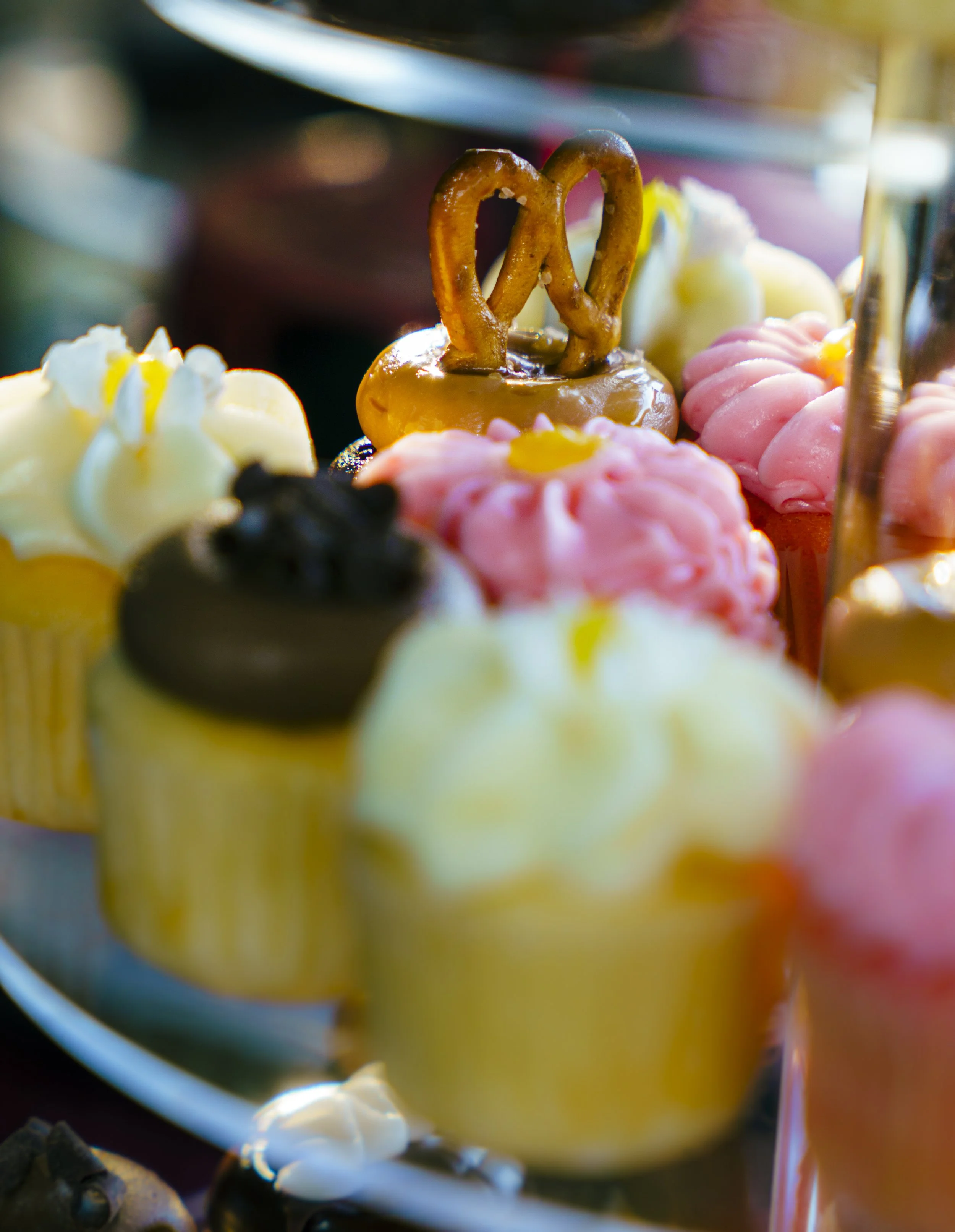 Close-up of a baked pretzel mounted on a dessert with pink and white frosting and other desserts in the background.
