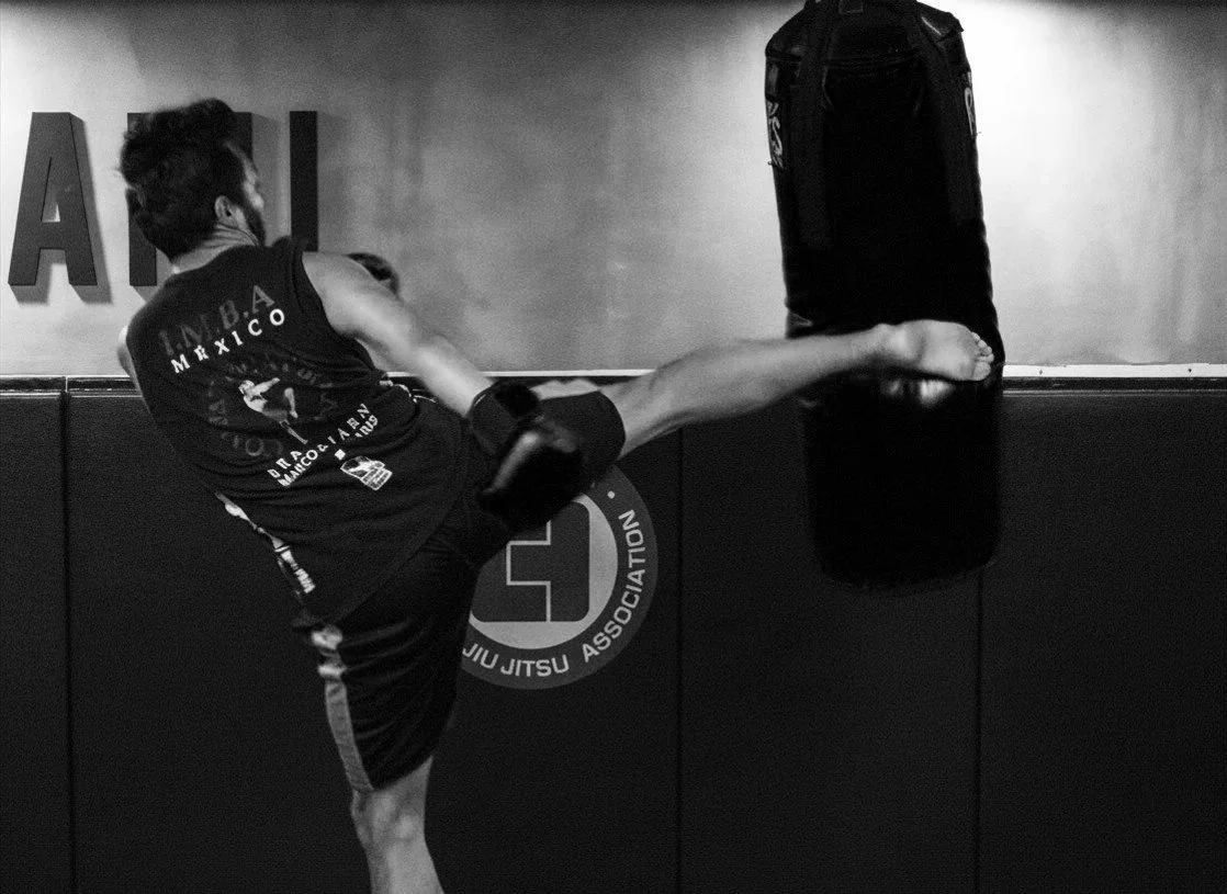 Persona practicando kicking en un saco de boxeo en un gimnasio.