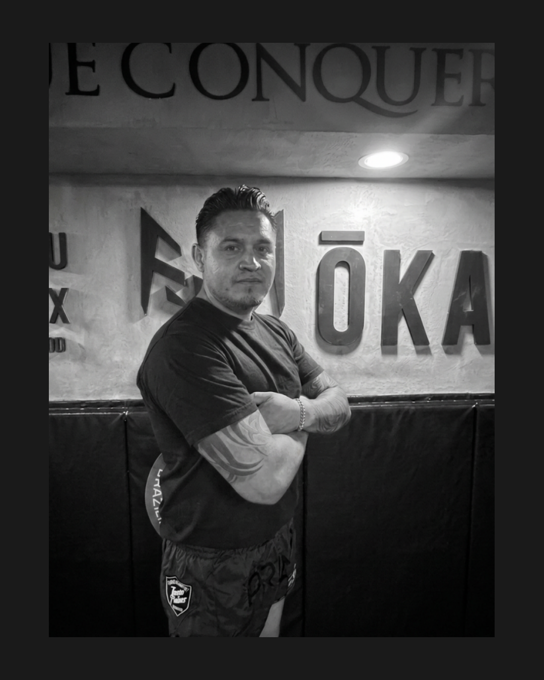Kru de Muay Thai certificado posando frente al muro principal de la academia de combate ŌKAMI en México.