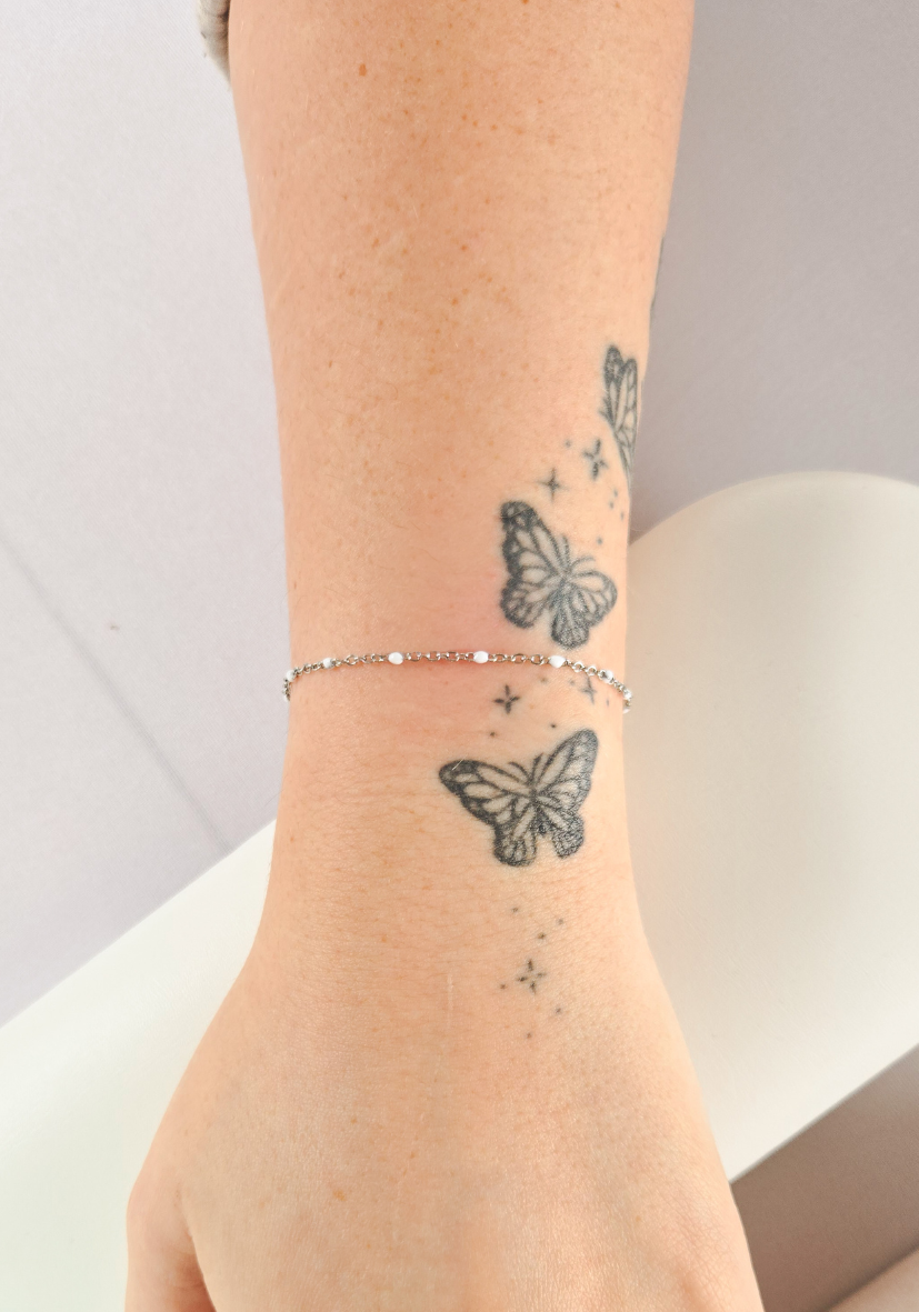 Close-up of a person's wrist with butterfly tattoos and a silver bracelet.