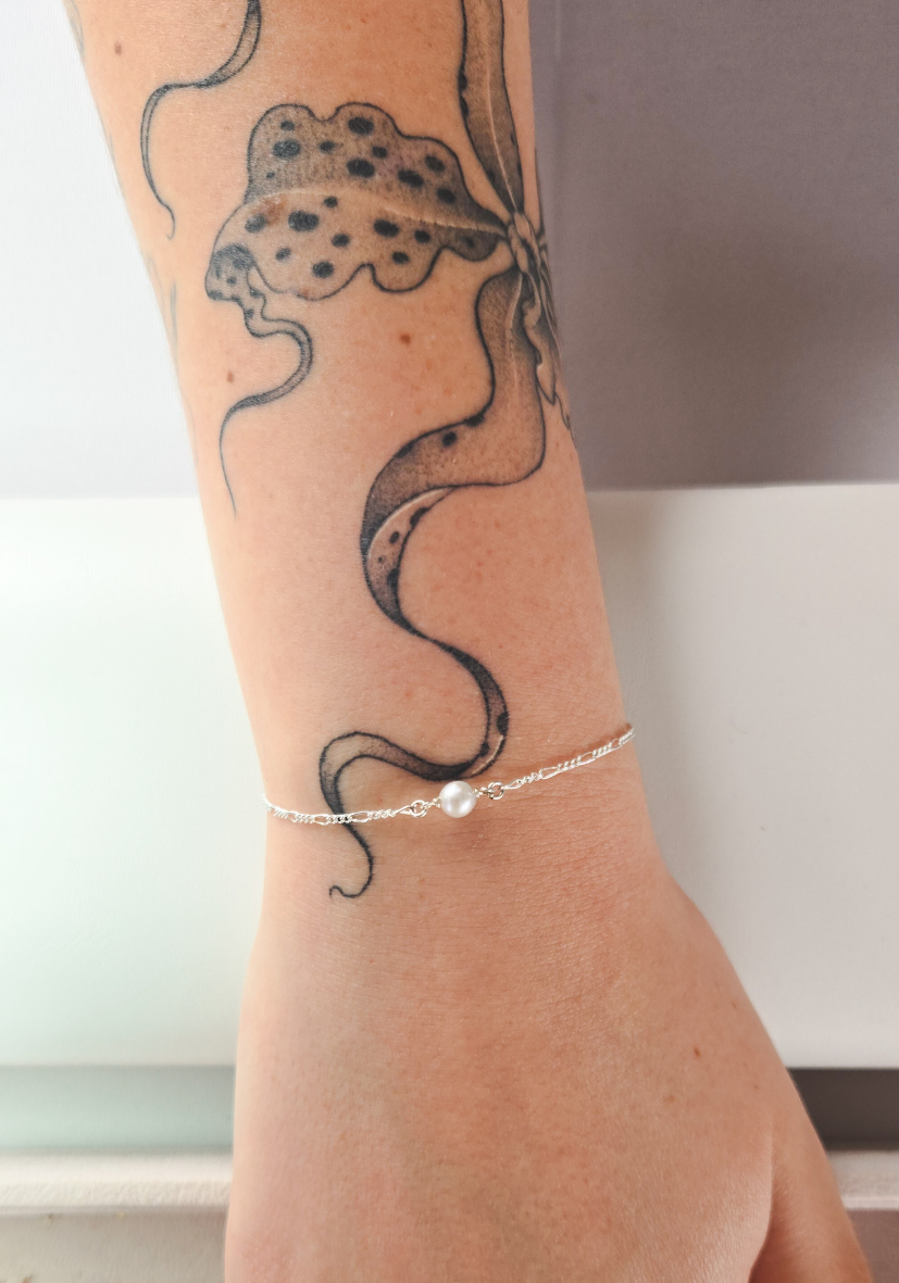 Tattoo of a snake on a person's forearm, with a bracelet featuring a white pearl on the wrist.