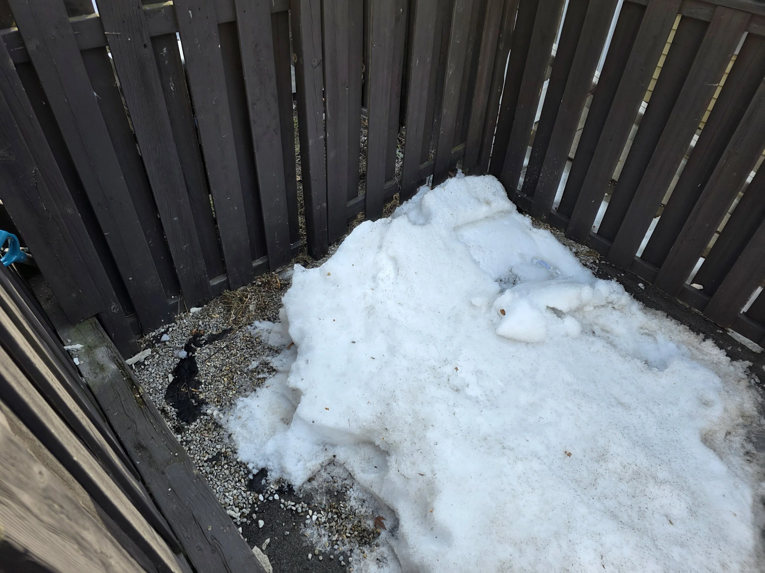 A small alleyway with a wooden fence on both sides and a patch of snow on the ground.