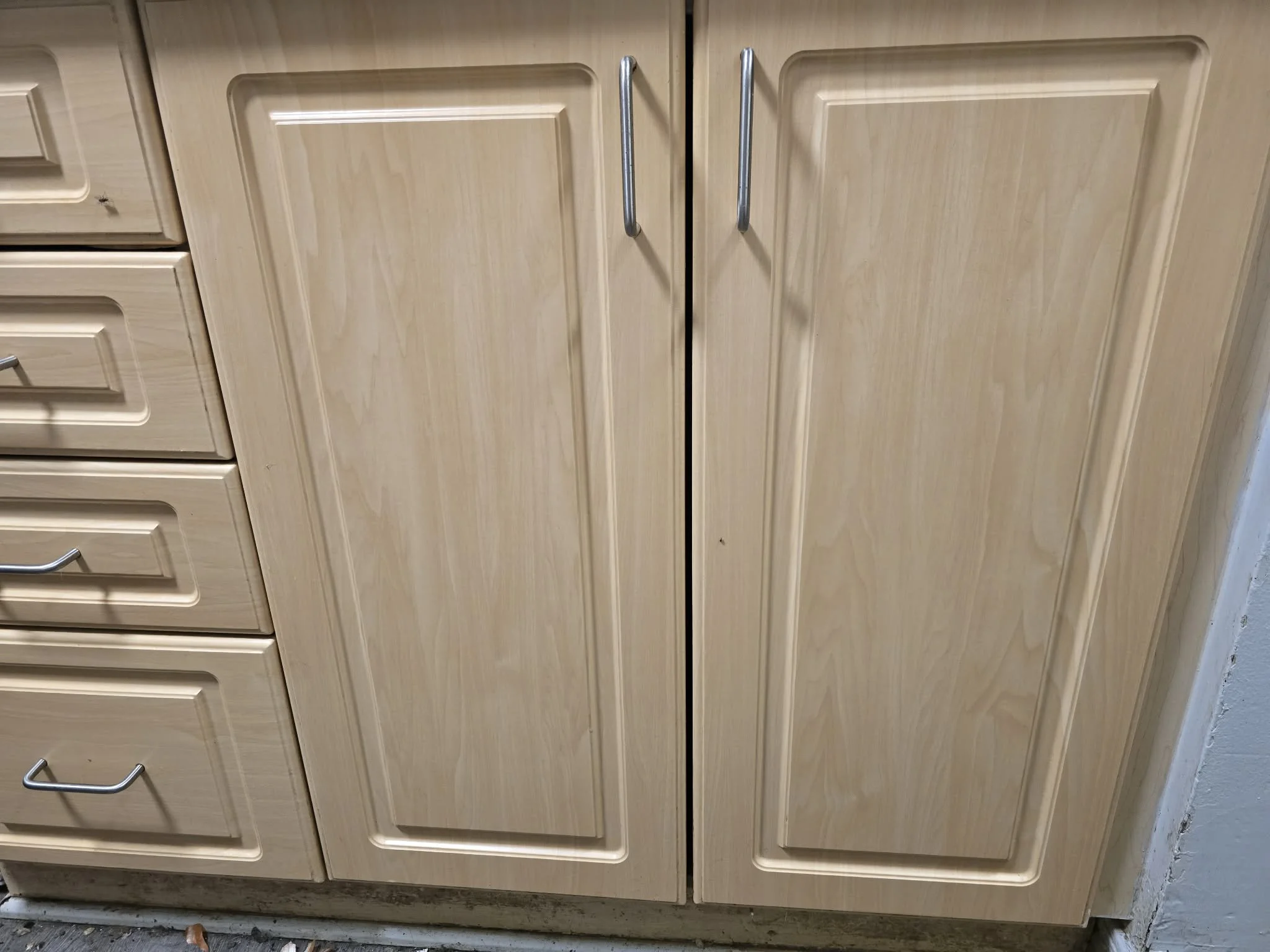 Wooden kitchen cabinets with silver handles on a light-colored cabinet door.