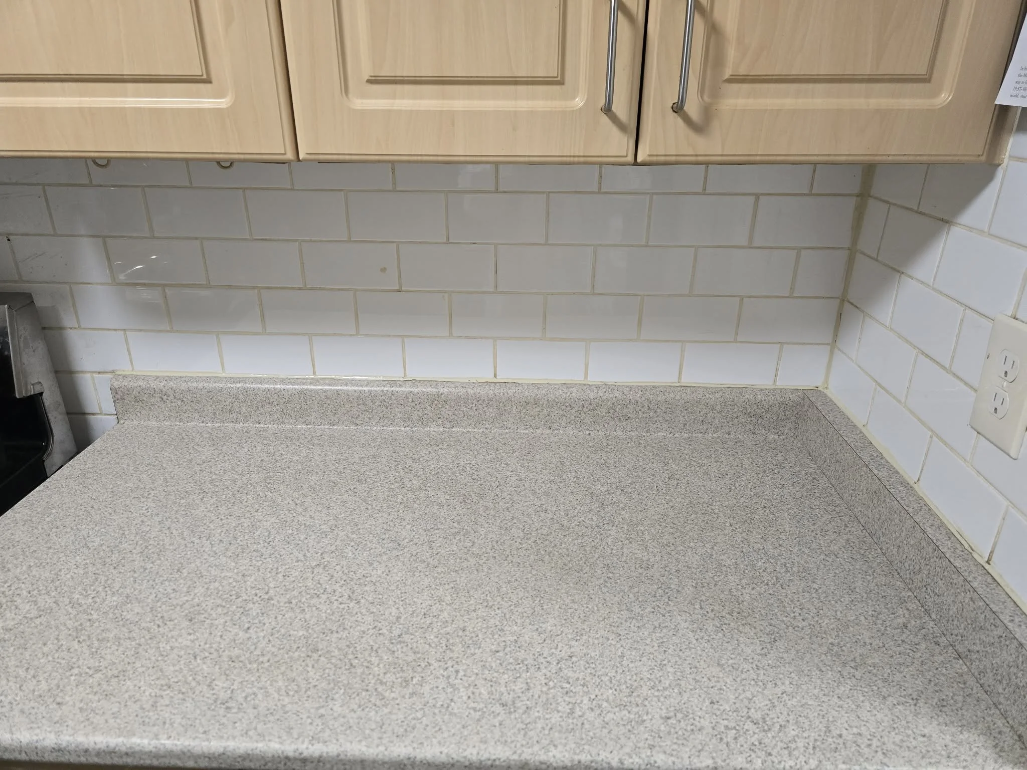 Kitchen with beige countertop, white tiled wall, and wooden cabinets.