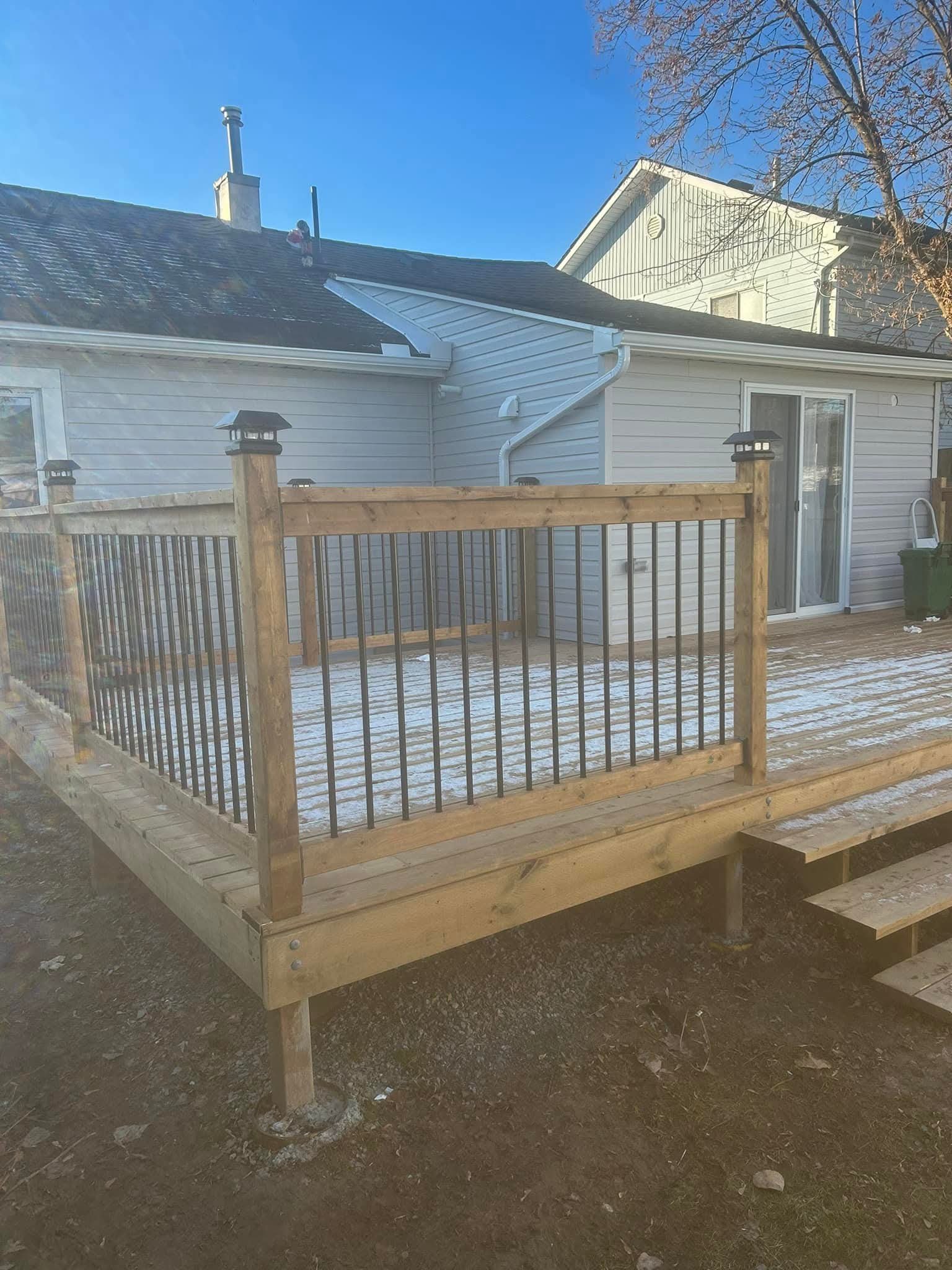 New wooden deck built outside a house with white siding, a sliding glass door, and a brown wooden fence with black lantern-style light fixtures on top of fence posts.