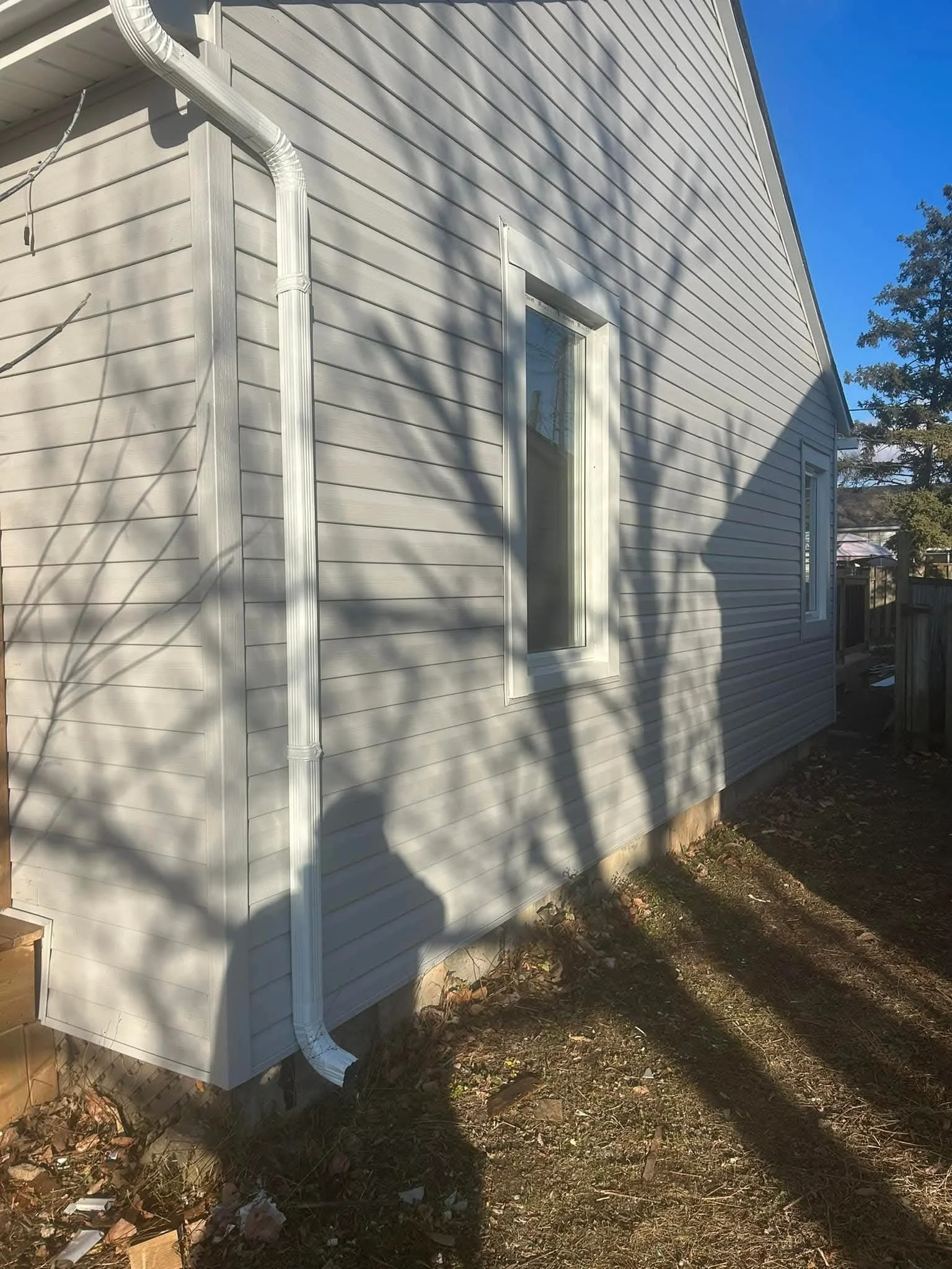 The exterior of a house showing beige siding, two windows, and a white downspout on a sunny day.