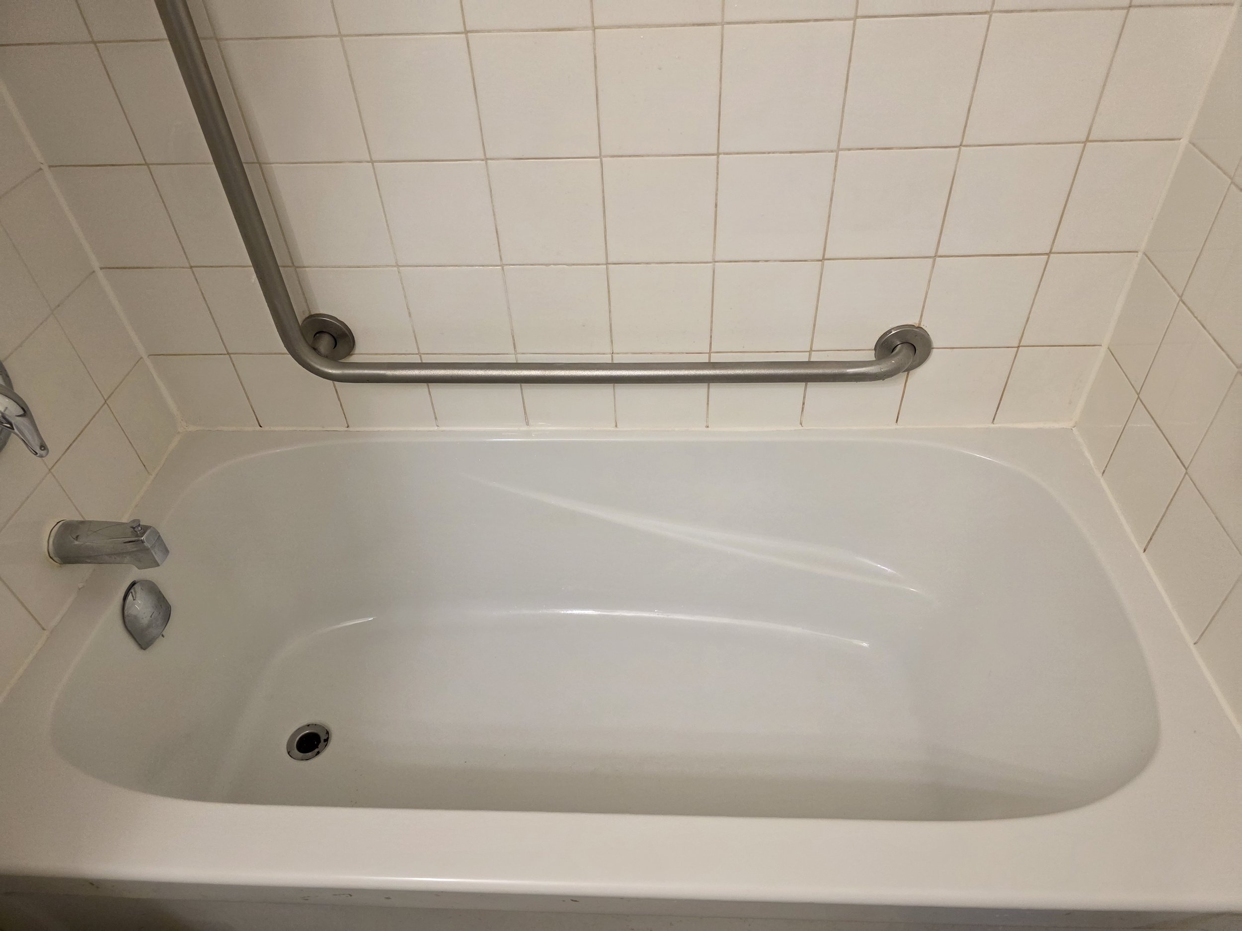 A white bathtub with a silver grab bar mounted on a tiled wall above it.