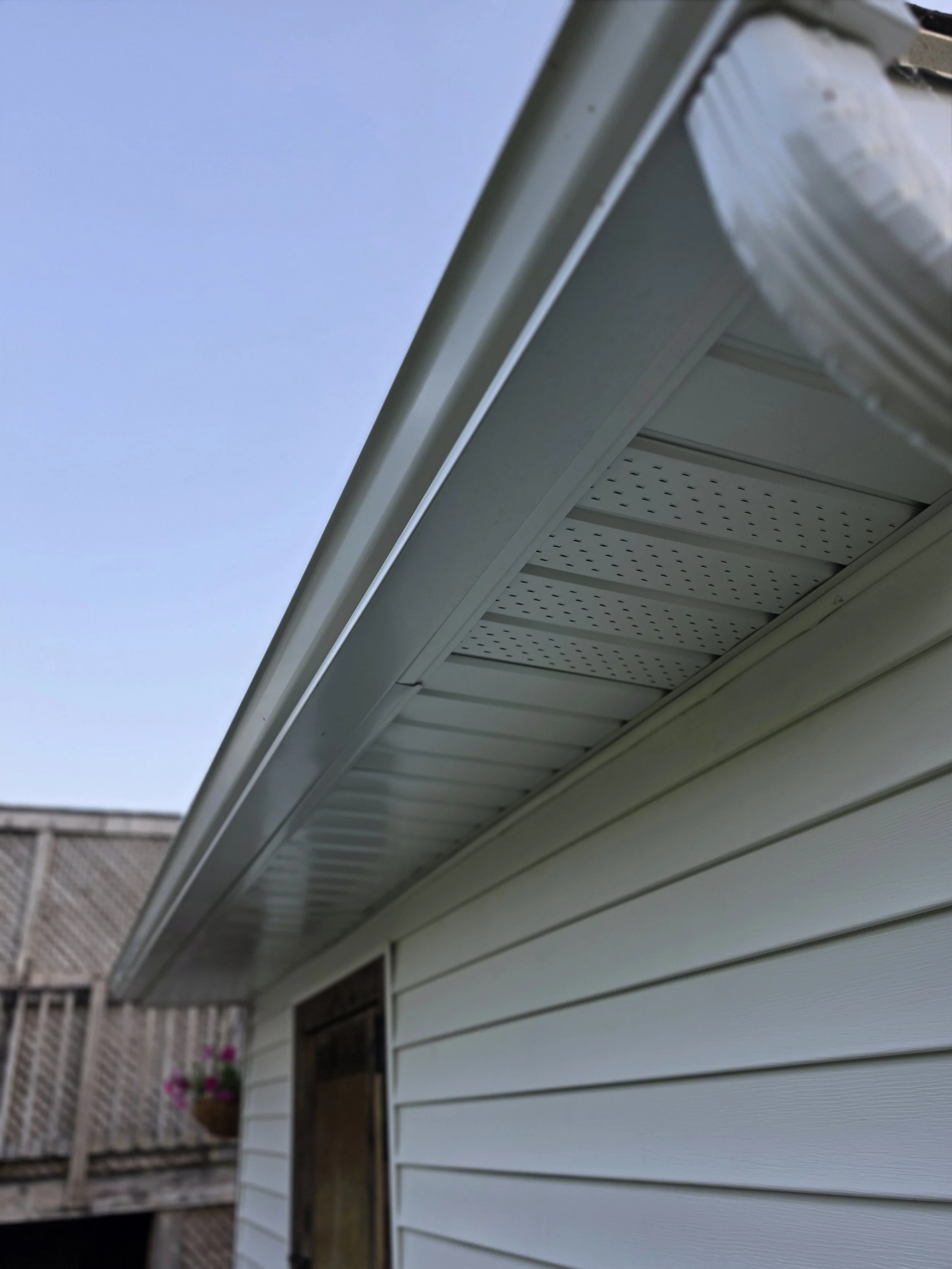 Close-up of a house exterior showing white siding, a white gutter, and a clear blue sky above.