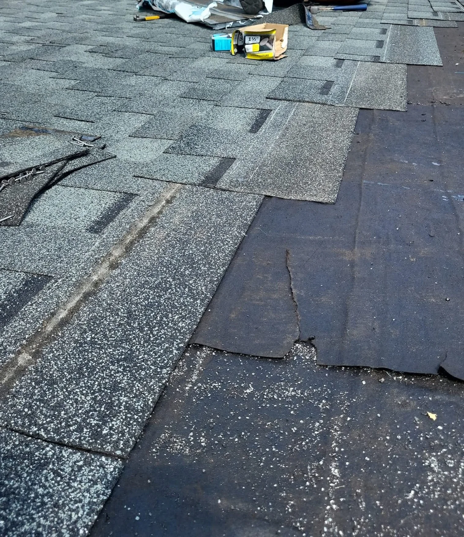 A roofing project where asphalt shingles are being installed on a roof, with tools and materials scattered around.