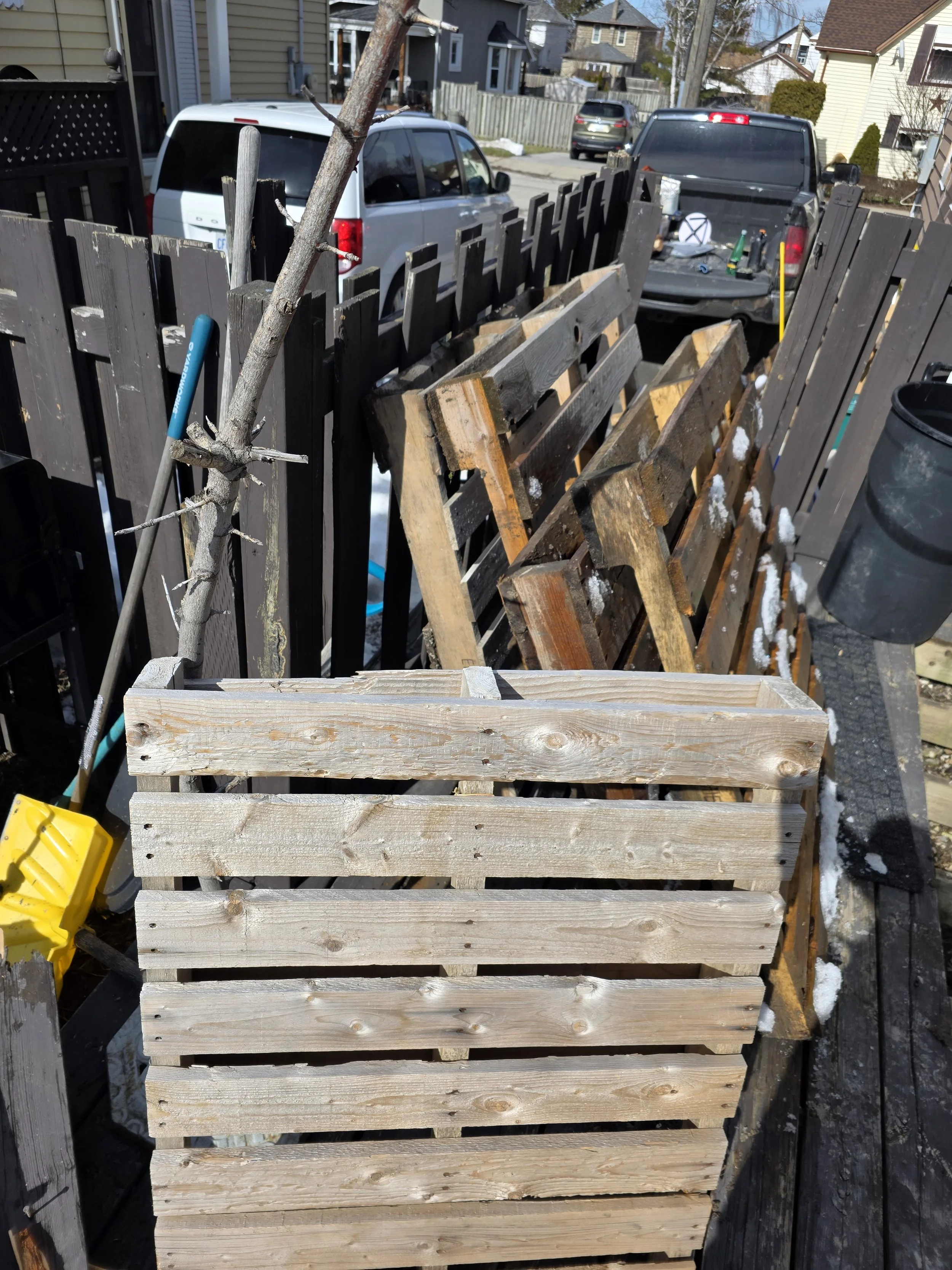 Image of a partially assembled wooden fence with some sections completed and others still being built, with backyard and parked cars in the background.