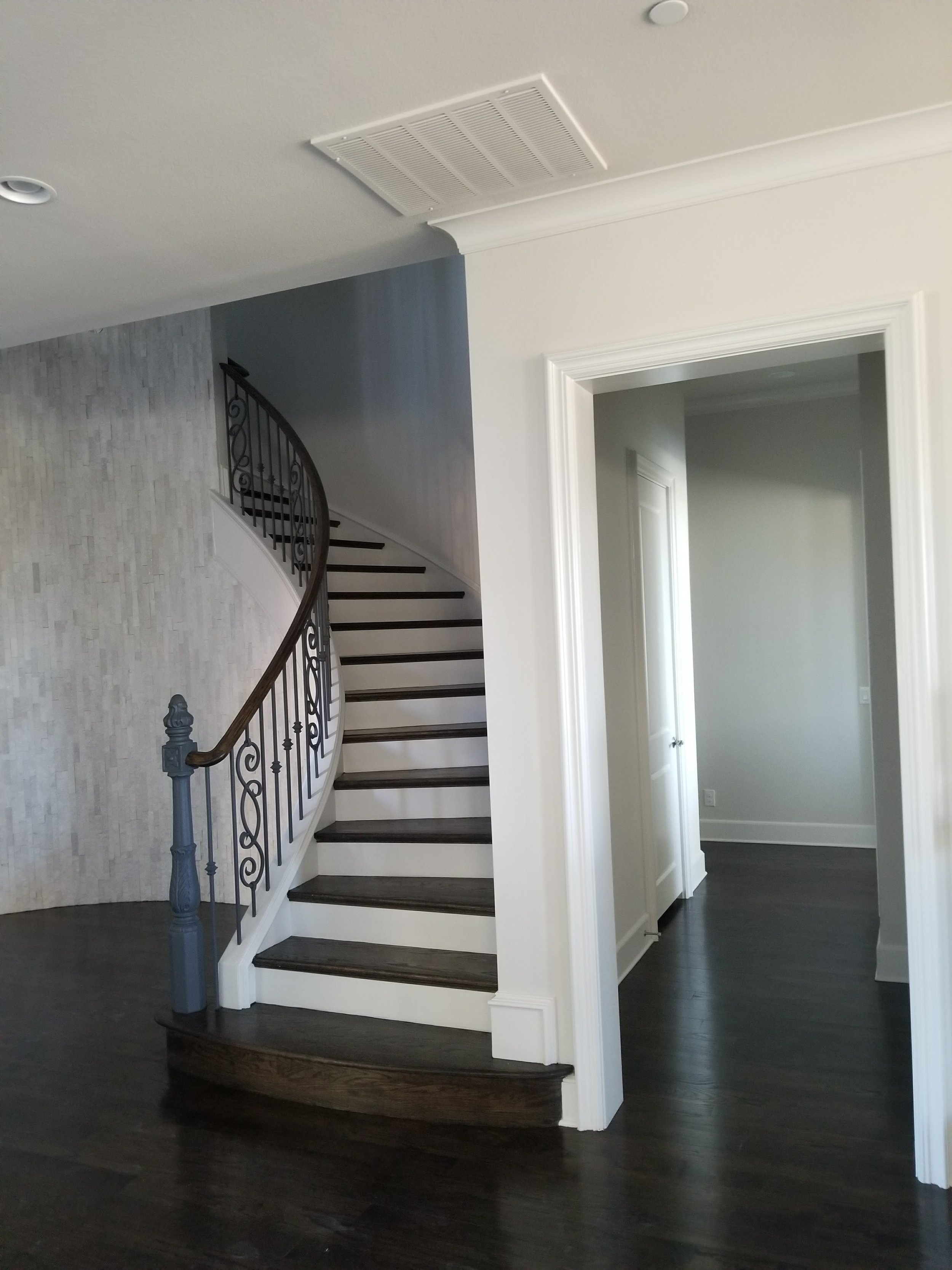 Custom curved staircase with hardwood treads, white risers and iron balusters beside a light accent wall in a luxury home in Plano.