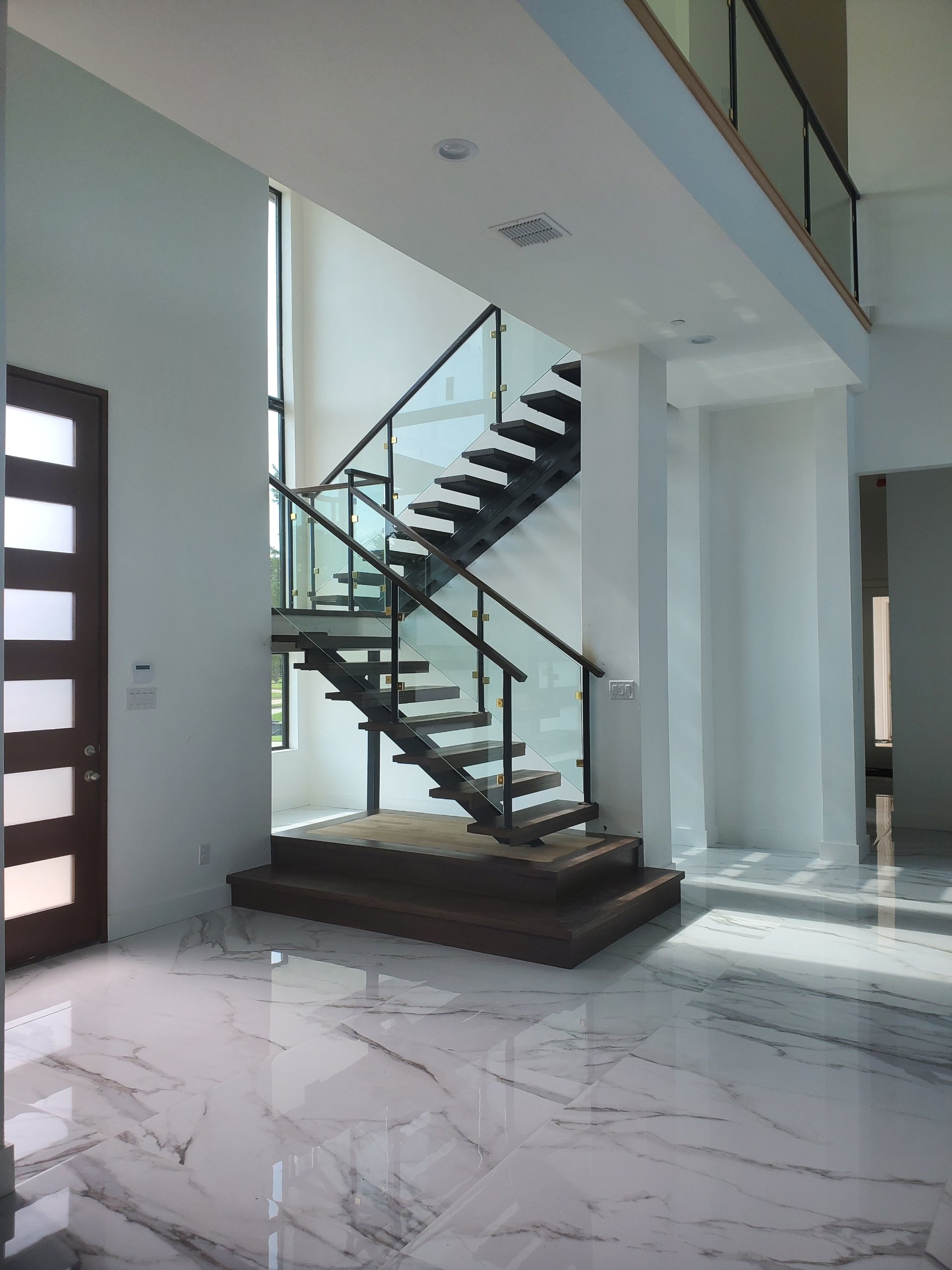 Interior shot of a modern custom home in Southlake, complete with a floating wood and glass staircase, along with polished marble flooring.