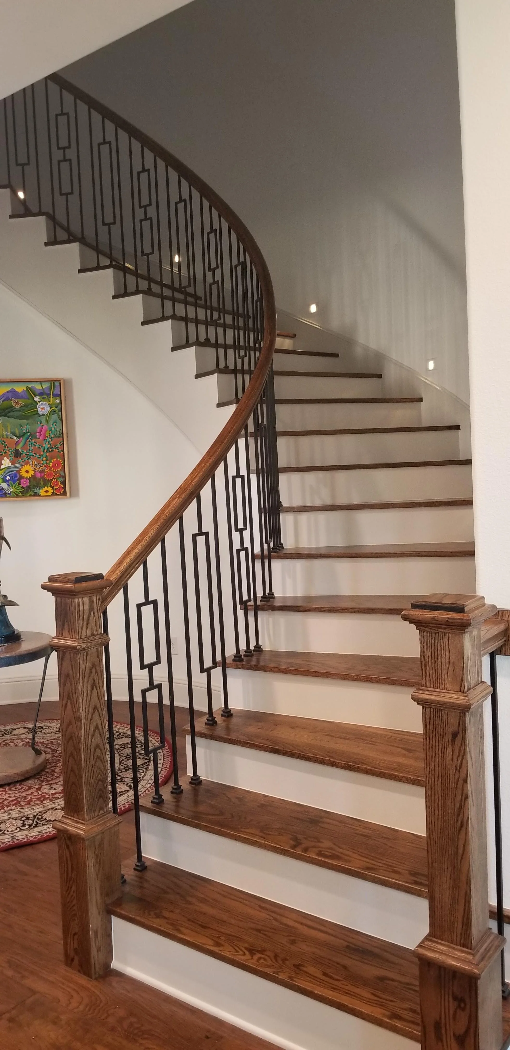 Luxury, custom grand staircase in Dallas featuring hardwood treads, white risers, iron balusters and a step lighting system.