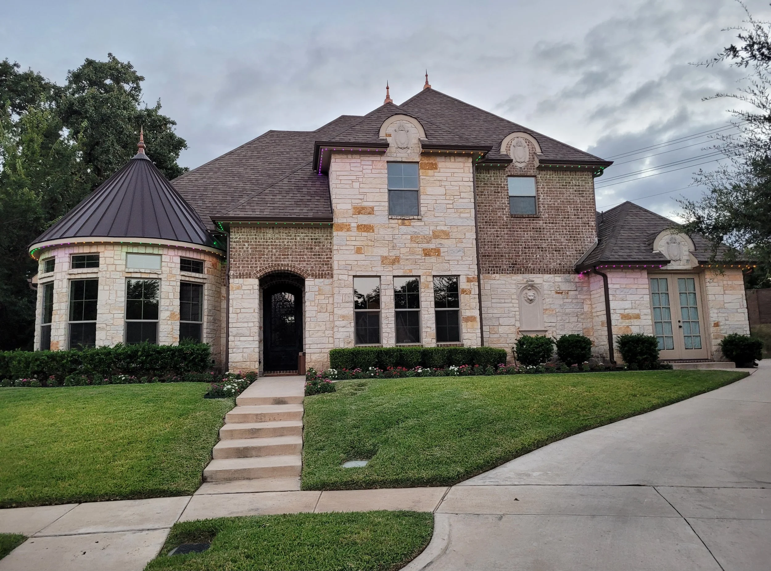 Outside shot of a custom luxury home built in Euless. It features a rotunda with a metal roof, custom and precisely laid stone and brickwork.