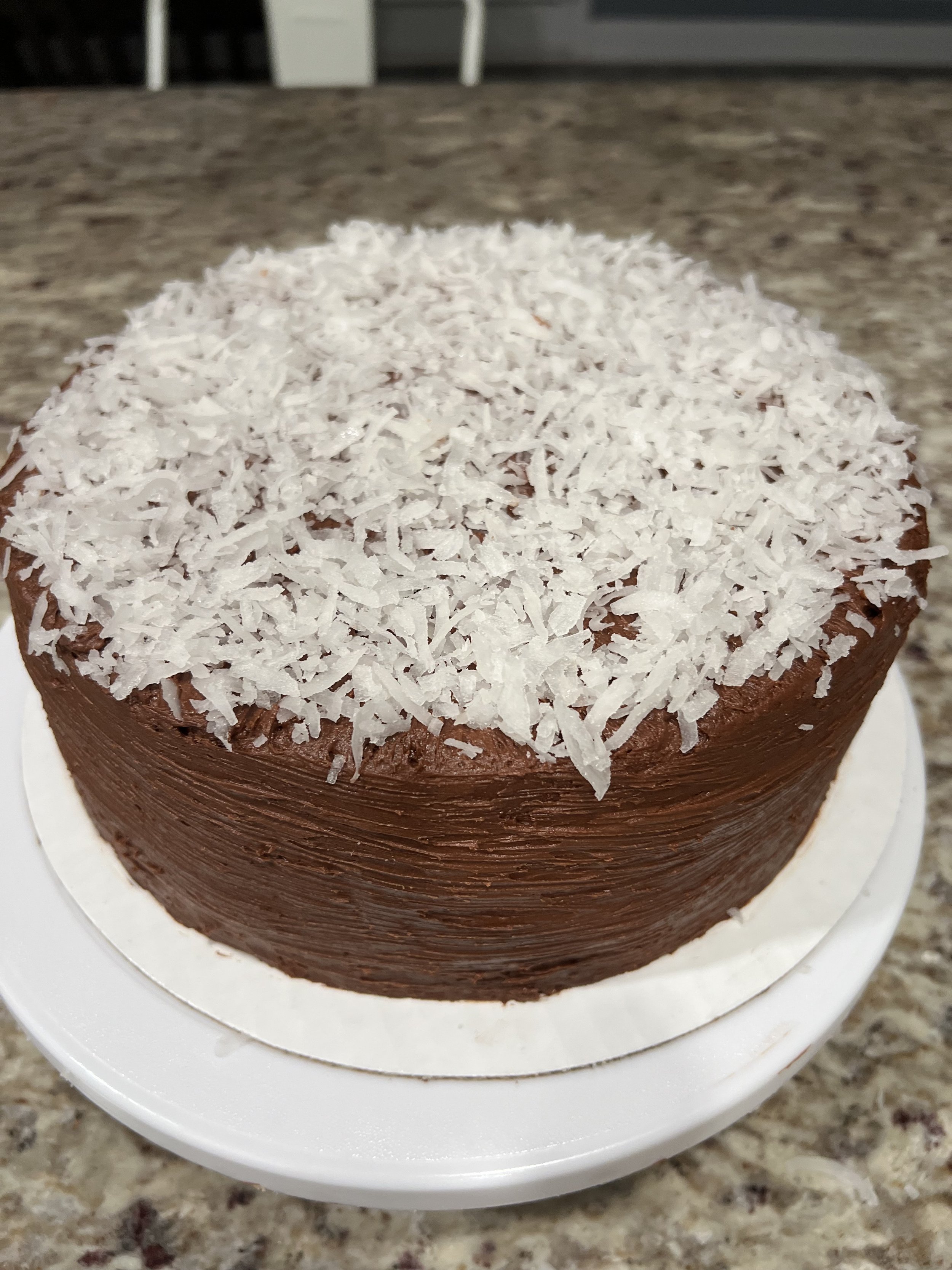 Chocolate cake topped with shredded coconut on a white cake stand.