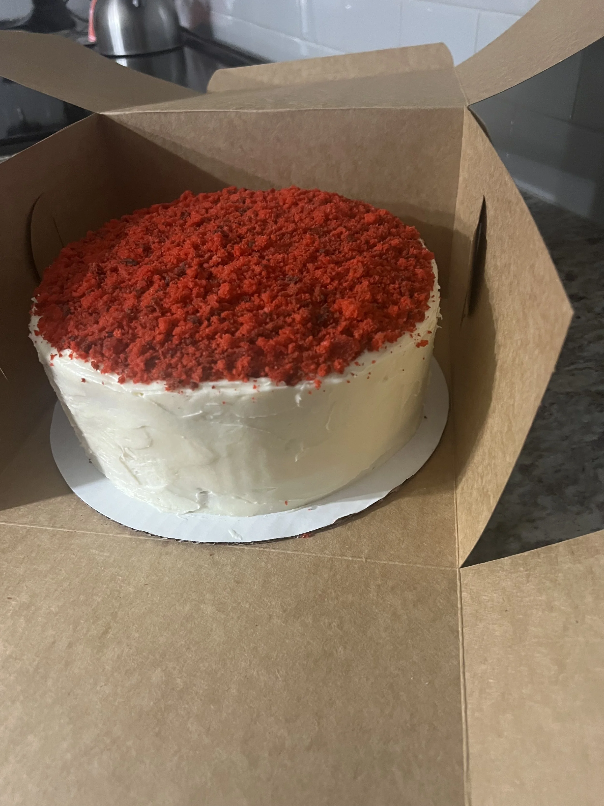 A cake inside a cardboard box on a brown counter.