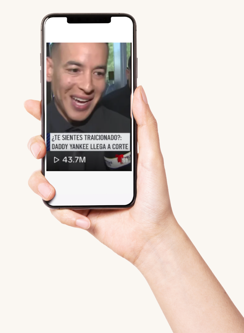 Hand holding a smartphone displaying a video with a smiling man and Spanish text, including a news logo and view count.