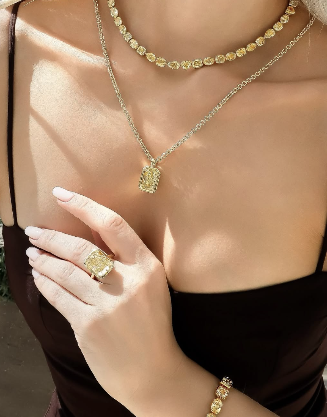 Close-up of a woman wearing gold jewelry, including a necklace, ring, and bracelet, with a focus on her hand and upper chest. Image from Weston Jewelers