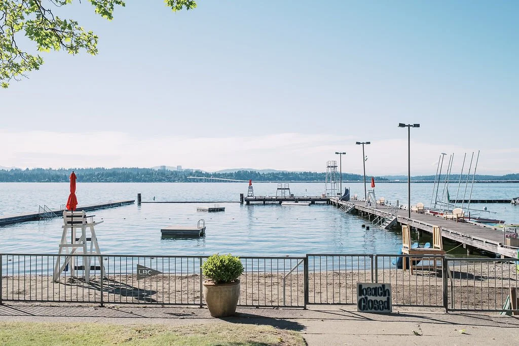 Empty dock on a calm lake with a lifeguard chair, a large potted plant, and a sign that says "Lawn Closed".