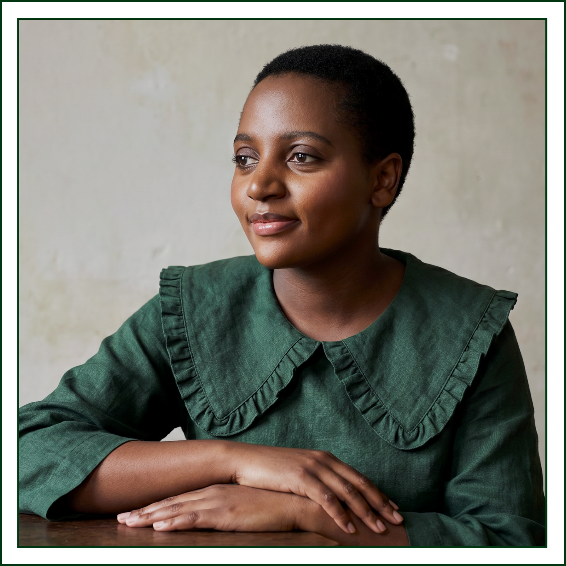 Square portrait of Lillian Ingabire, founder of Studio Kalili, an editorial branding studio in Chicago, seated at a wooden table in a green ruffle-collar linen top