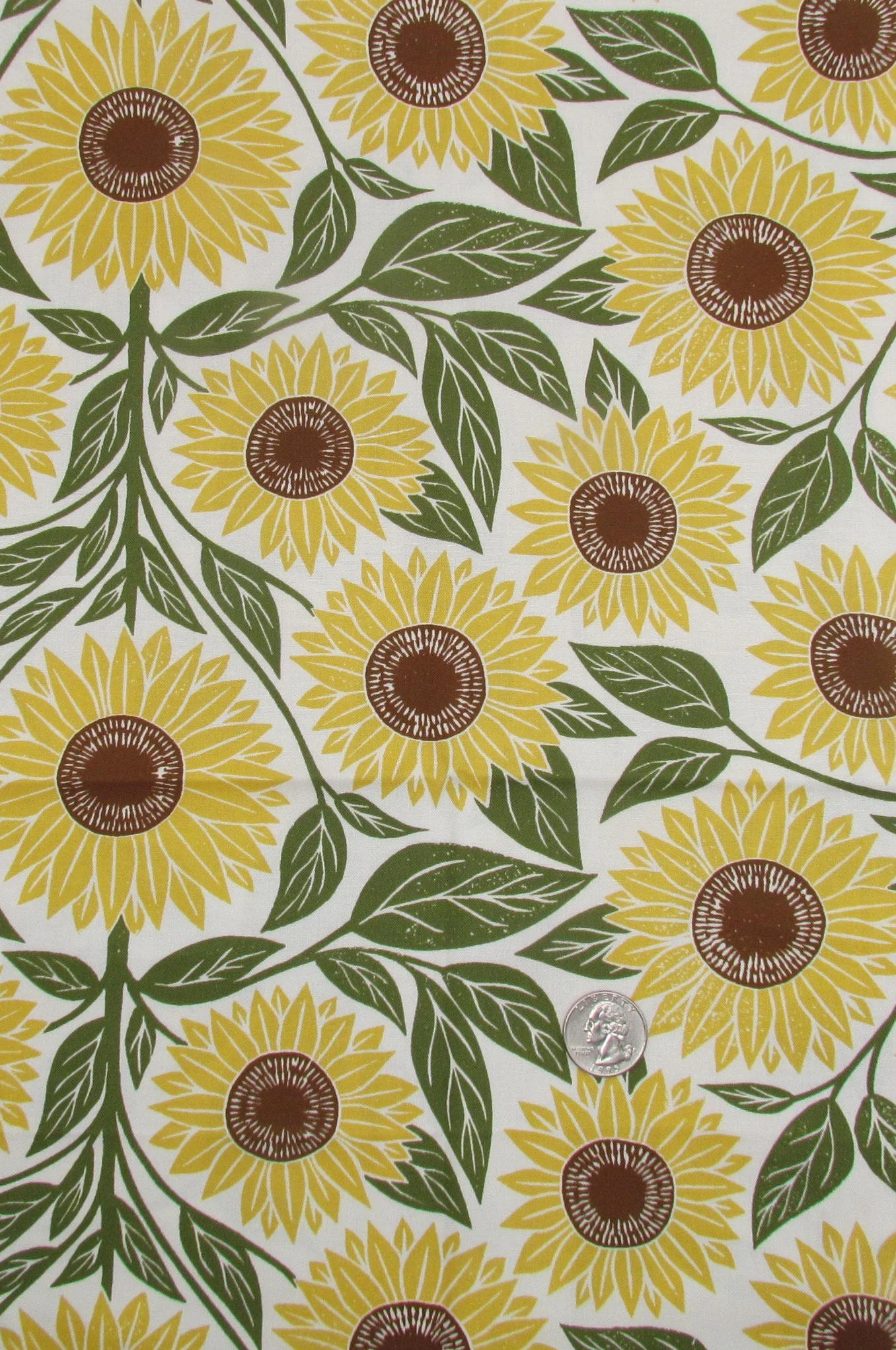 Pattern of yellow sunflowers with brown centers and green leaves on white background, with a quarter coin for size comparison.
