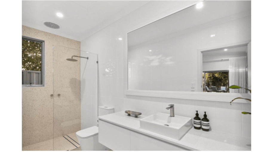 Modern bathroom with white walls, large mirror, white sink, black soap dispensers, minimalist decor, and a walk-in shower with a frosted glass door and a small window.