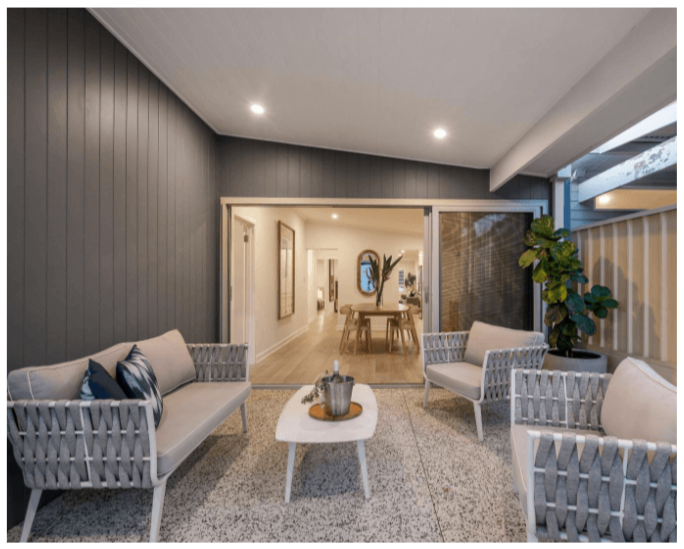Outdoor patio area with modern seating, a small coffee table, and a potted plant, leading into an indoor dining space.