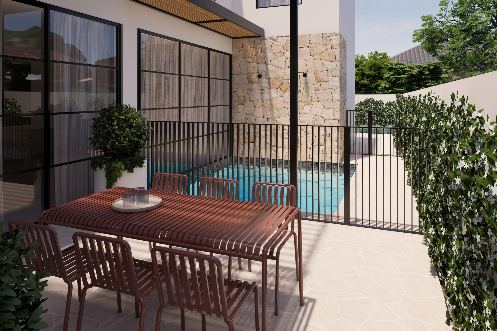A modern outdoor patio with a wooden dining table and chairs, a small pool, a stone wall, large glass windows with curtains, and trees in the background.