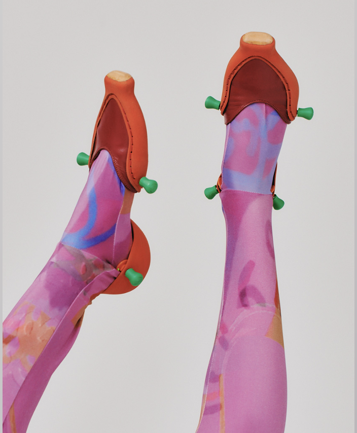 Two mannequin legs wearing colorful, abstract patterned pantyhose and orange shoe covers with green pins attached.