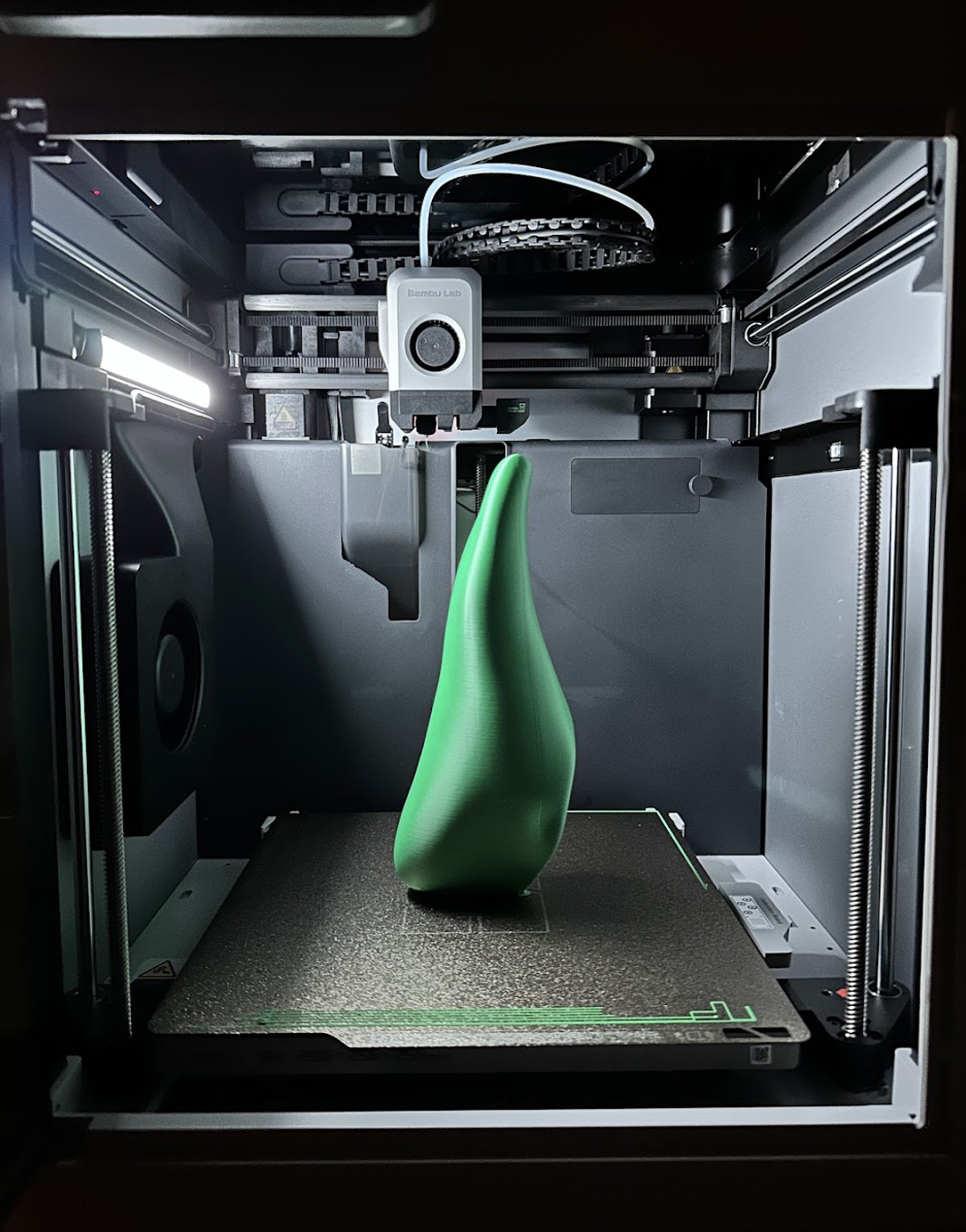 3D printer inside a machine with a green object being printed.