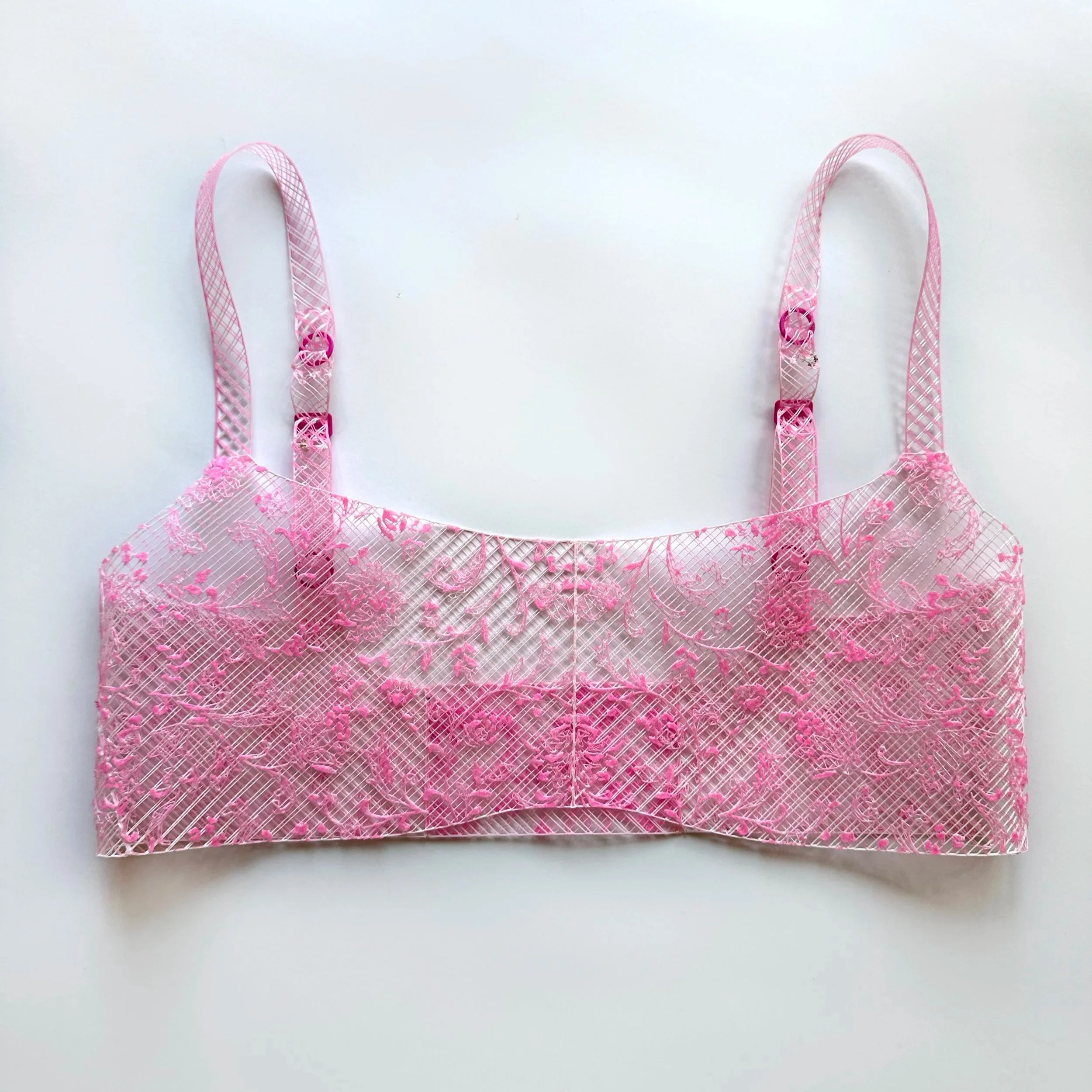 Pink lace lingerie top with thin straps, laid flat against a white surface.