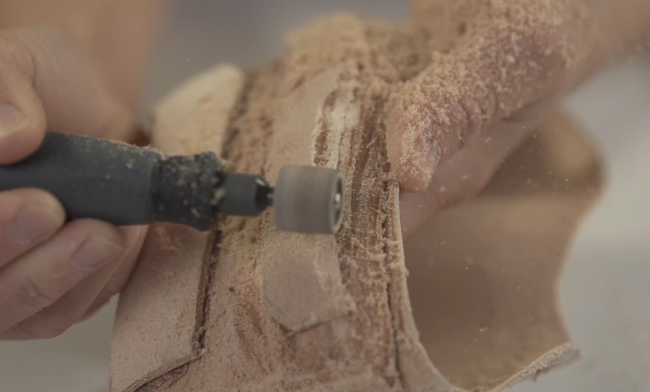 Hand carving wood with a rotary tool, creating detailed designs on a wooden piece.