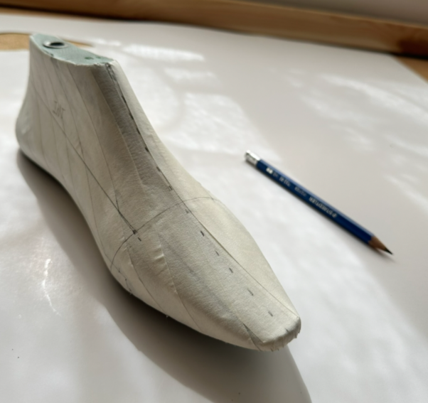 A fabric shoe last form on a white surface next to a blue mechanical pencil.