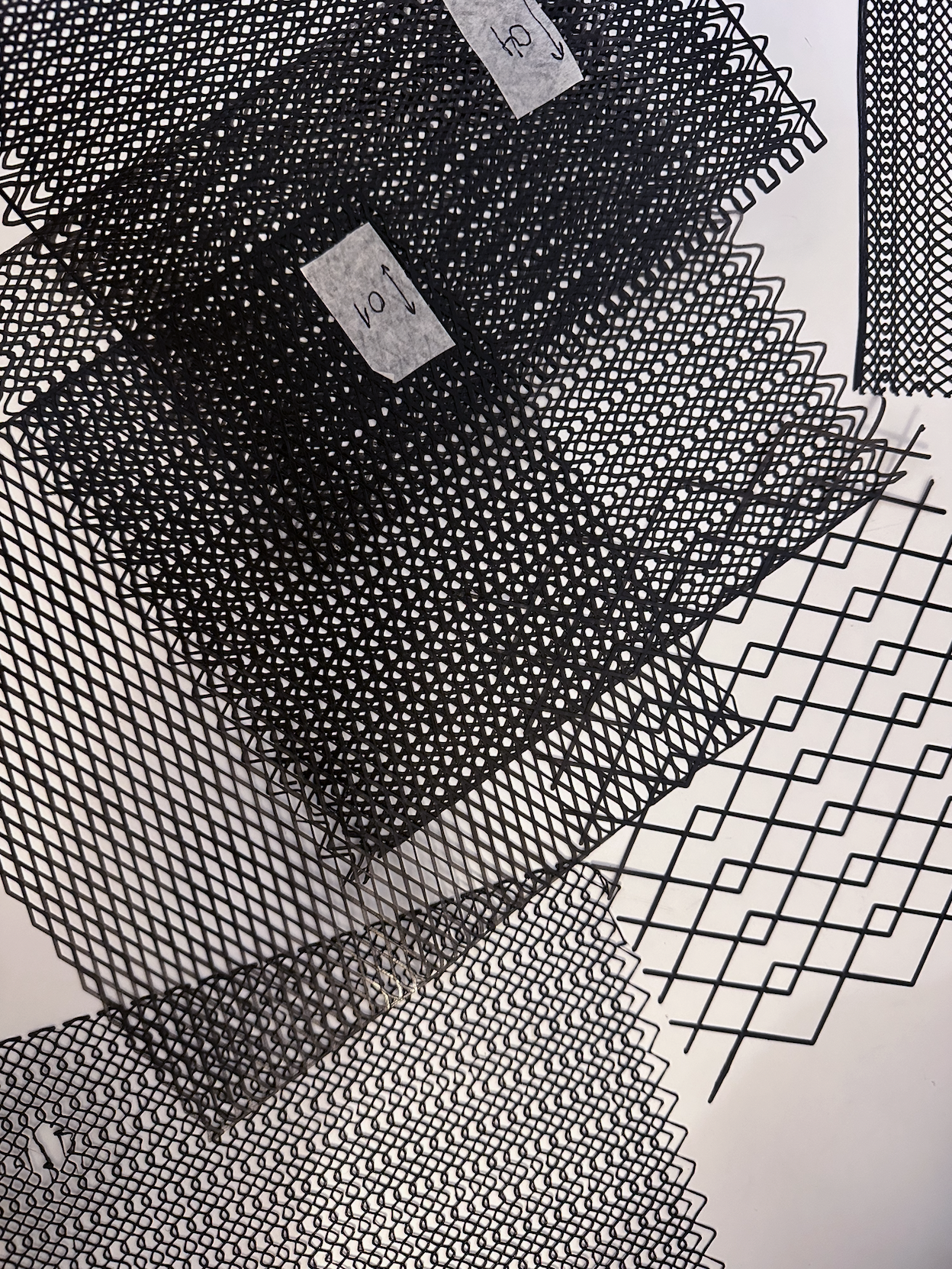 Multiple sheets of black mesh screen material with different grid patterns stacked on top of each other for craft or industrial use.