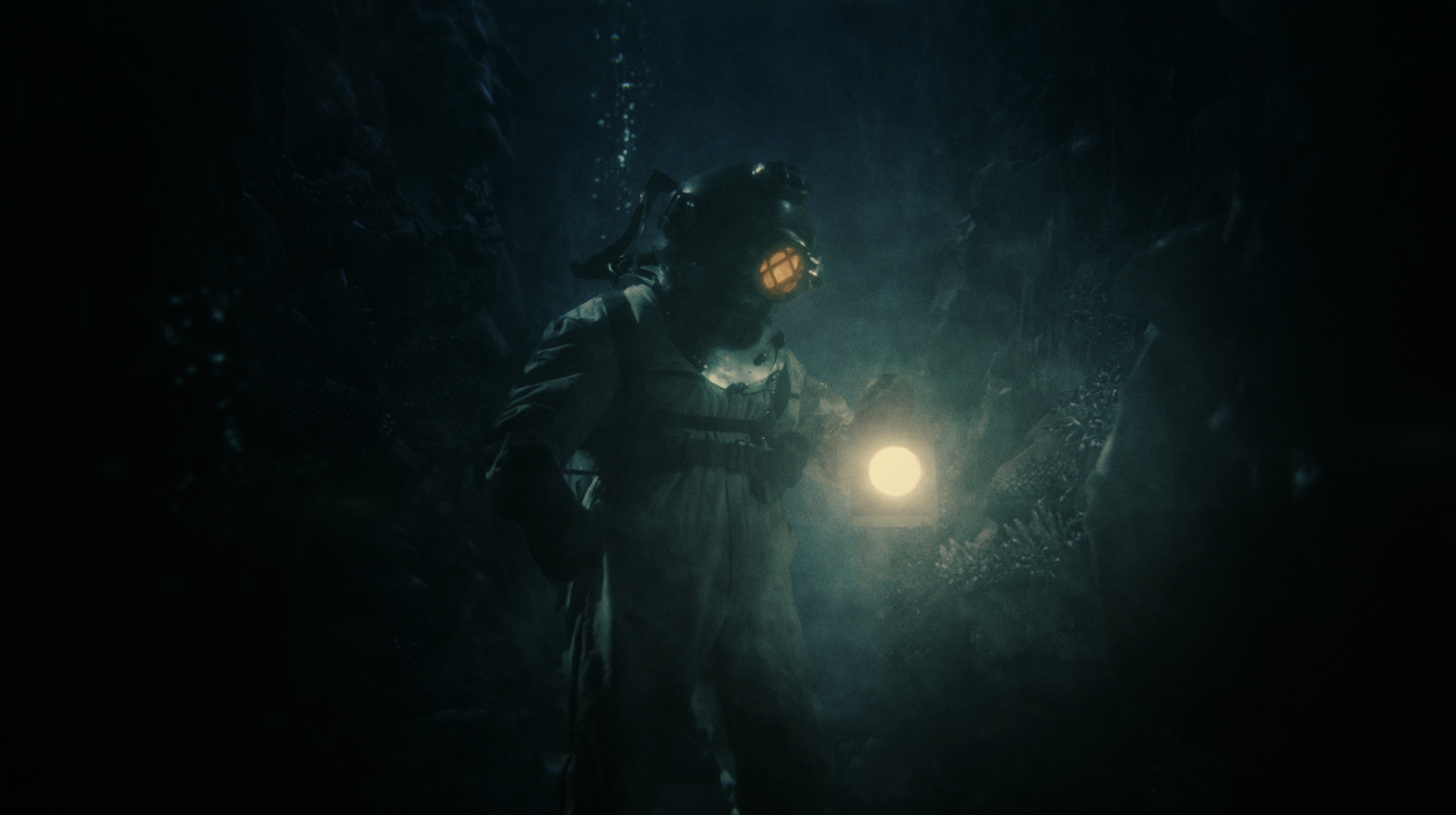 An explorer in a deep underwater cave is wearing a helmet with a light, exploring the dark, rocky environment.