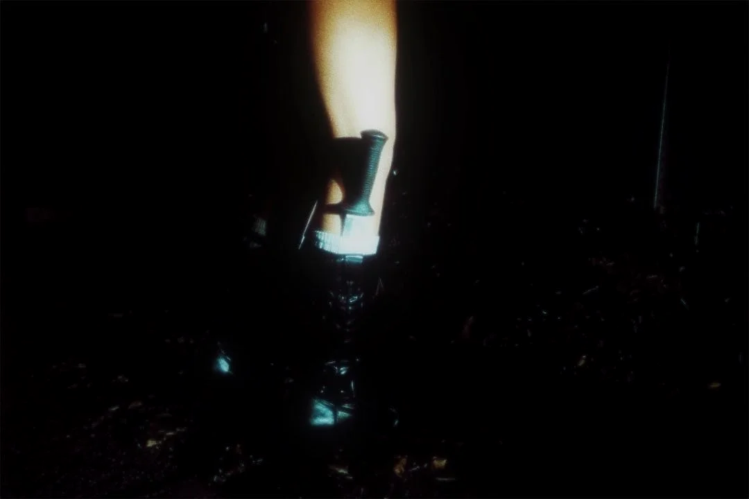 A lighter on the ground in front of a gun holster attached to a person's belt, with the person's hand in the background, in a dark environment.