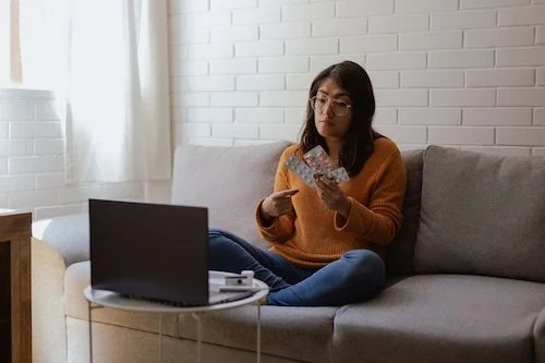 Woman holding up medications to her computer on a telemedicine visit working with Unscripted Medicine to deprescribe medications and regain her health