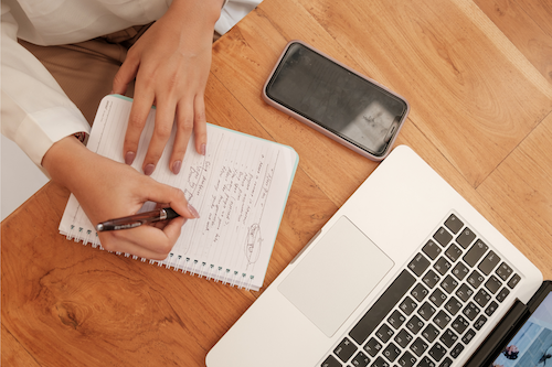 Computer and phone with person taking notes during a comprehensive functional medicine telehealth visit with Unscripted Medicine