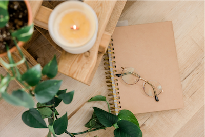 Glasses on a journal next to a plant and candle symbolizing intentional living and wellness in Alaska via telehealth